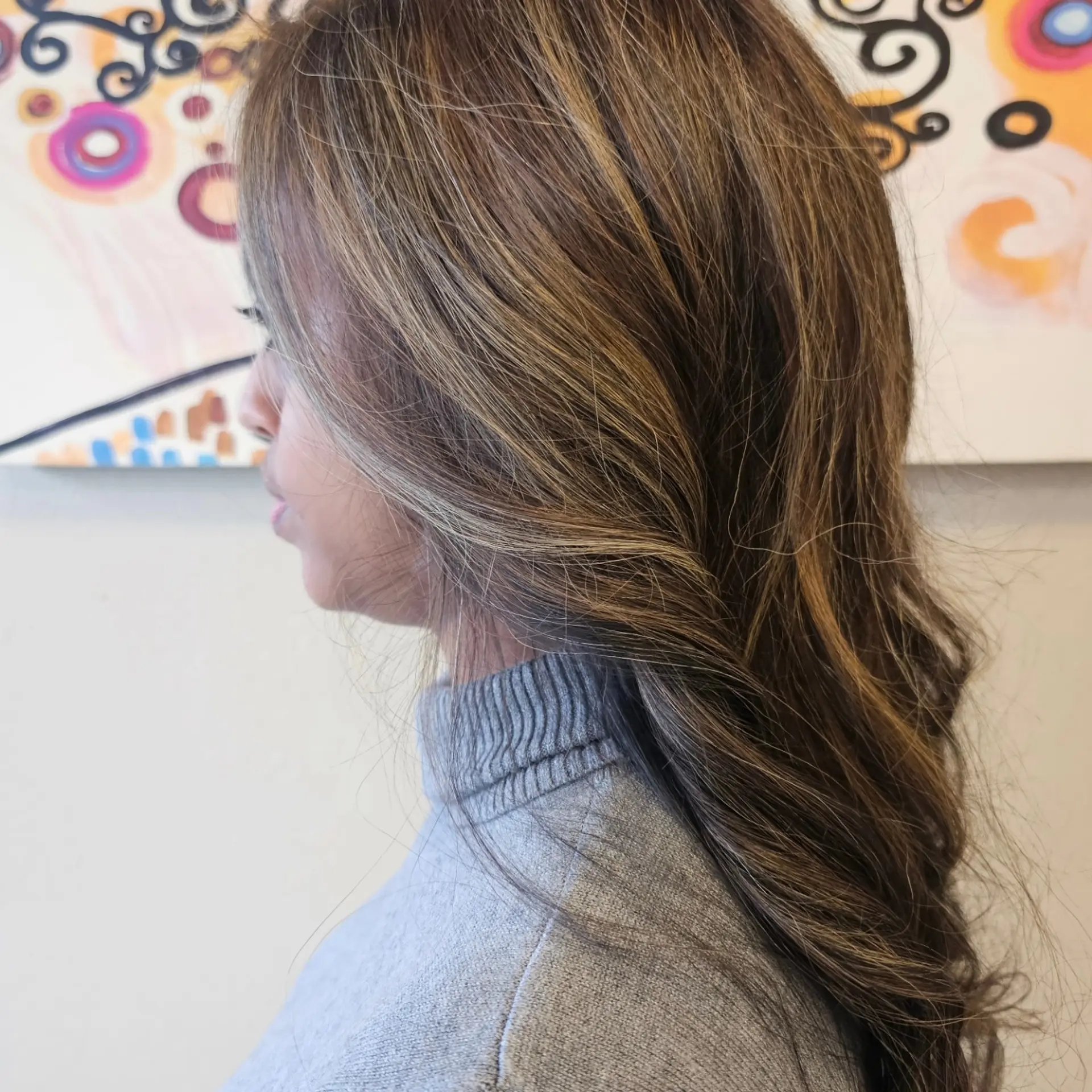 Side view of long brunette hair styled in loose waves with fine ash blonde highlights throughout. 1
