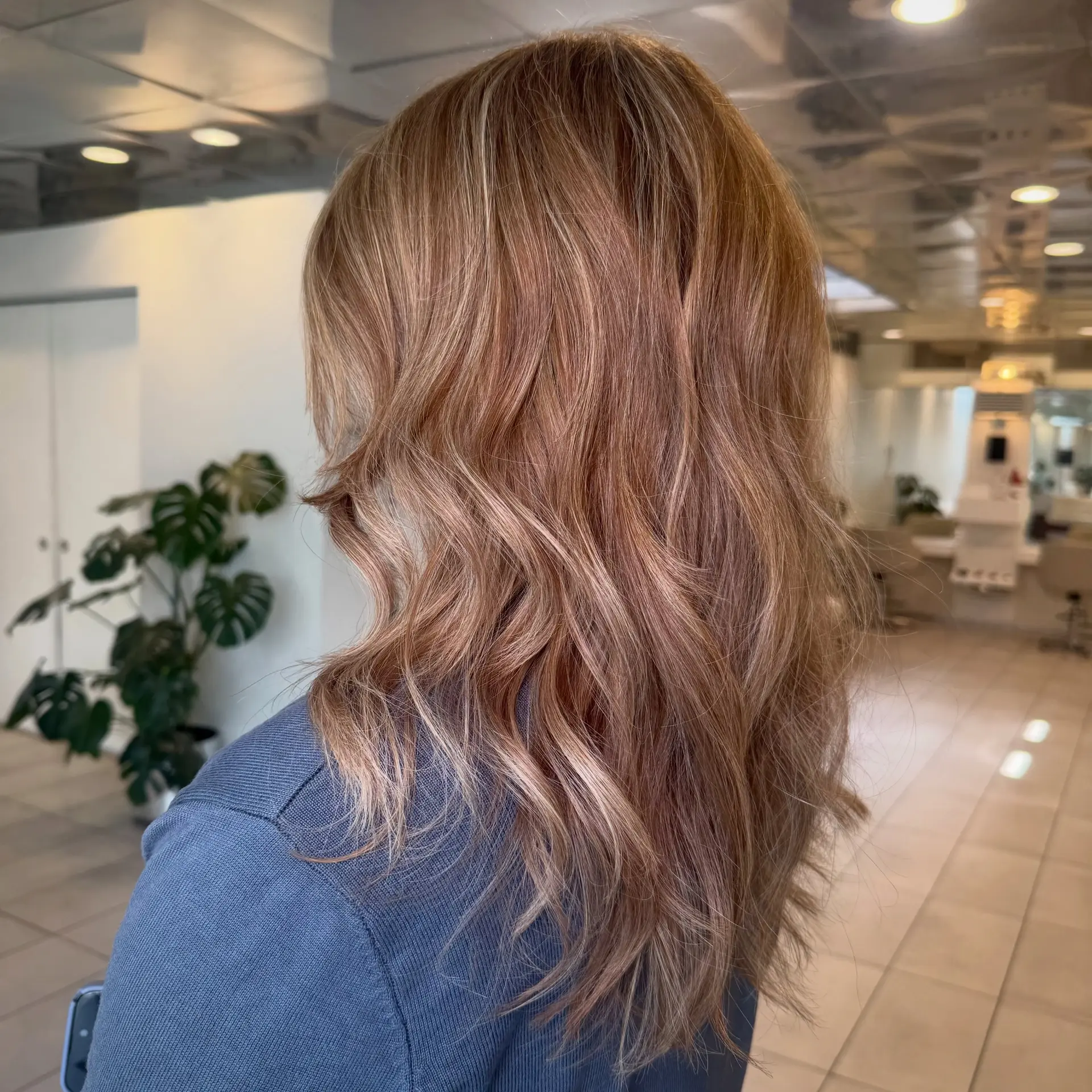 Medium-to-long layered hair styled in soft, cascading waves with multi-dimensional warm bronde highlights. 1