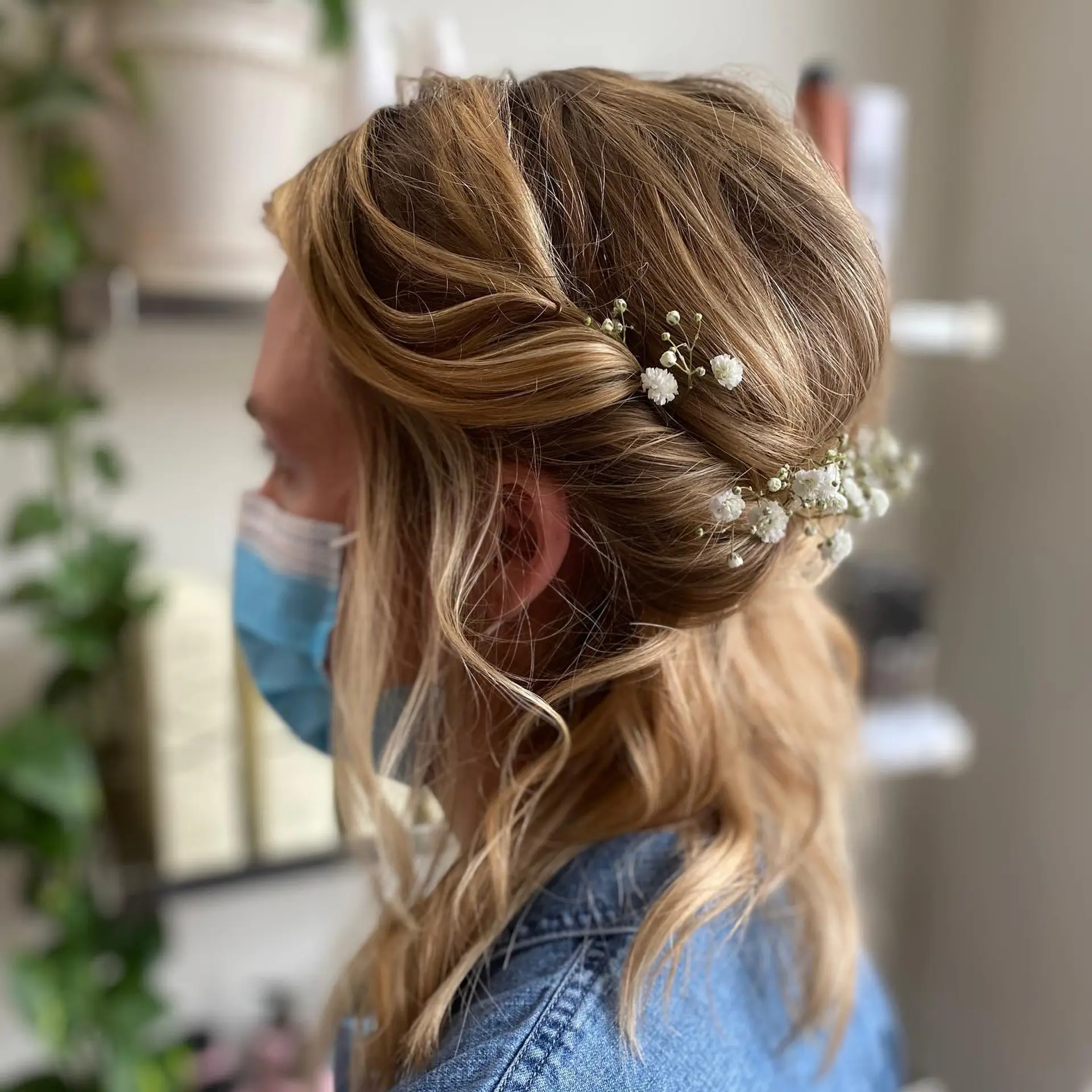 A romantic half-up bridal hairstyle featuring soft twists pinned at the back, adorned with delicate baby's breath flowers and loose, face-framing wavy tendrils. 1