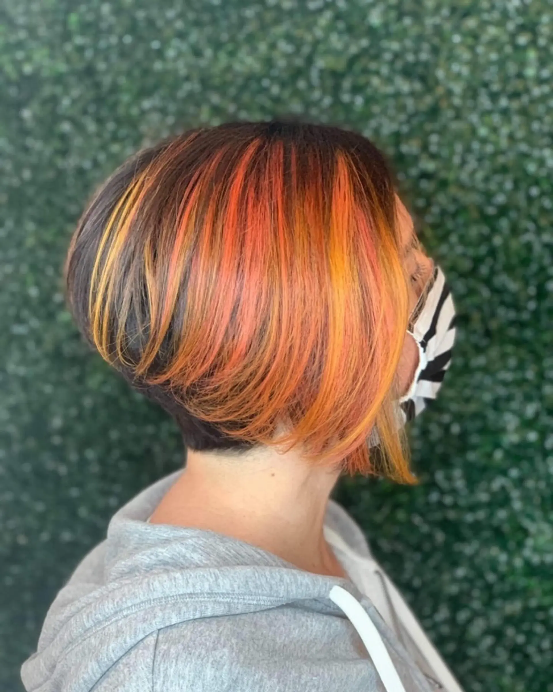 A short, stacked inverted bob featuring a dark brown base accented with vibrant sunset-orange and yellow highlights. 1