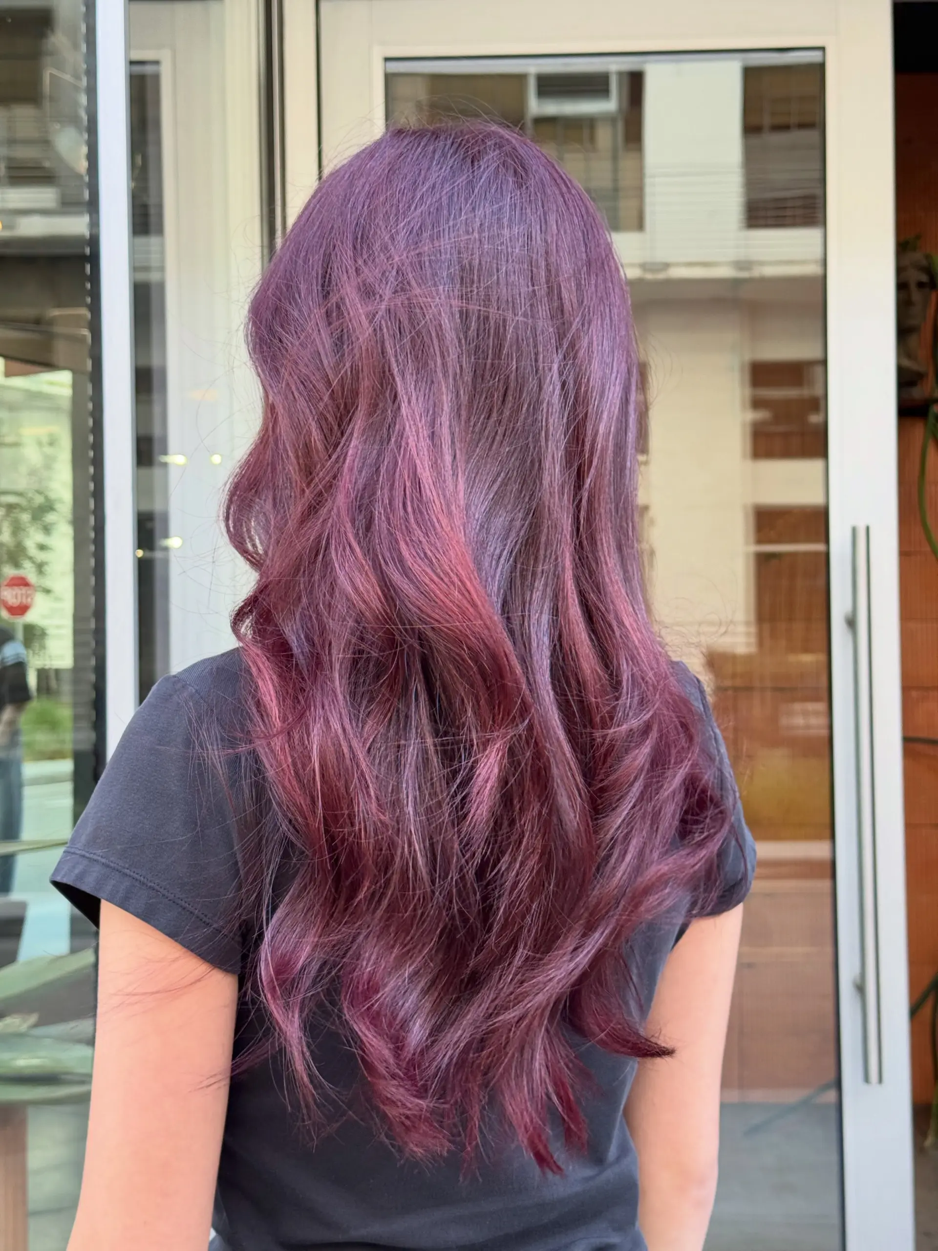Long layered hair colored in vibrant cherry red and violet tones, styled with loose, polished waves. 1
