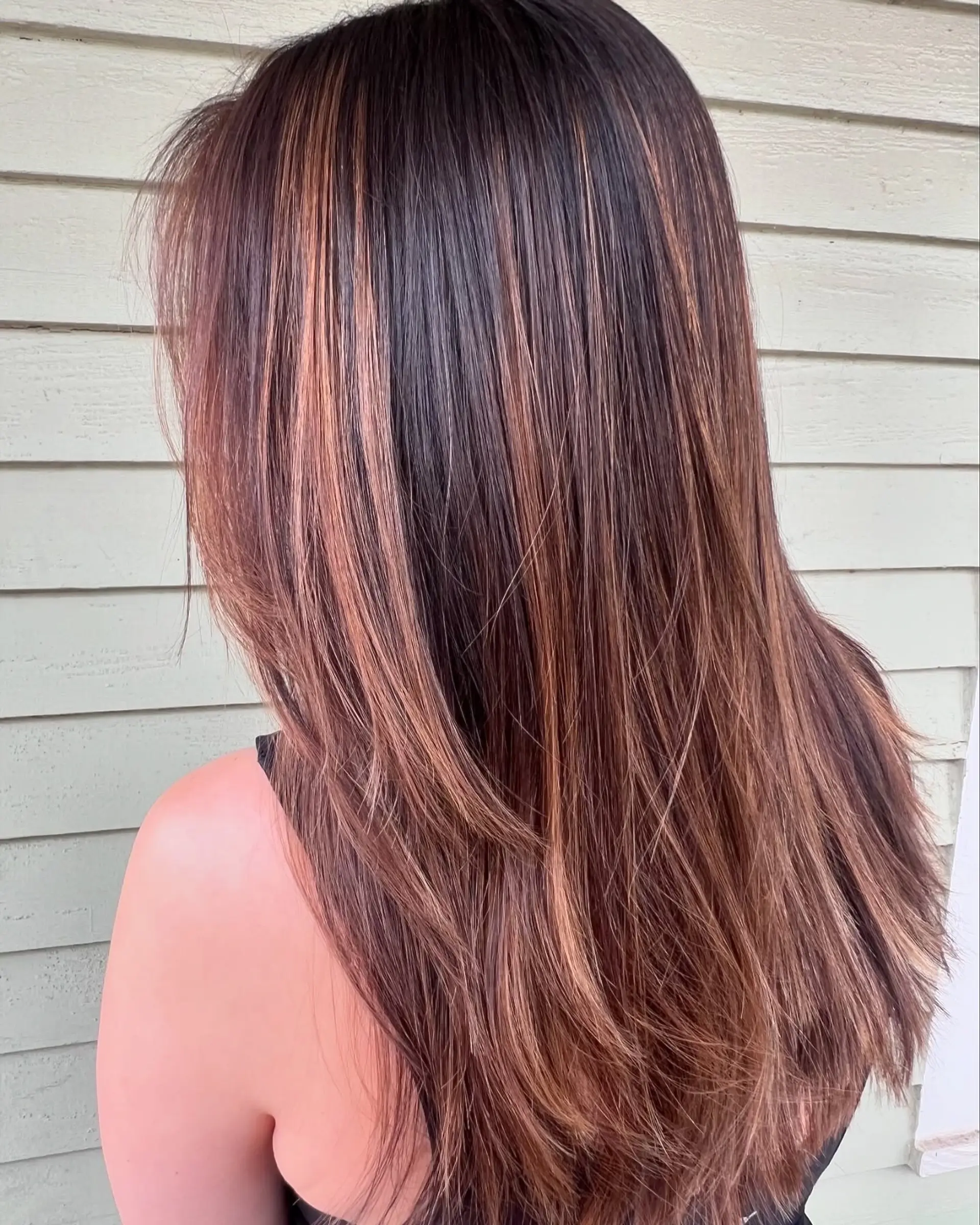 Long, straight hair styled with subtle layers and accentuated by warm caramel and golden-brown balayage highlights, offering a dimensional and sunkissed effect. 1