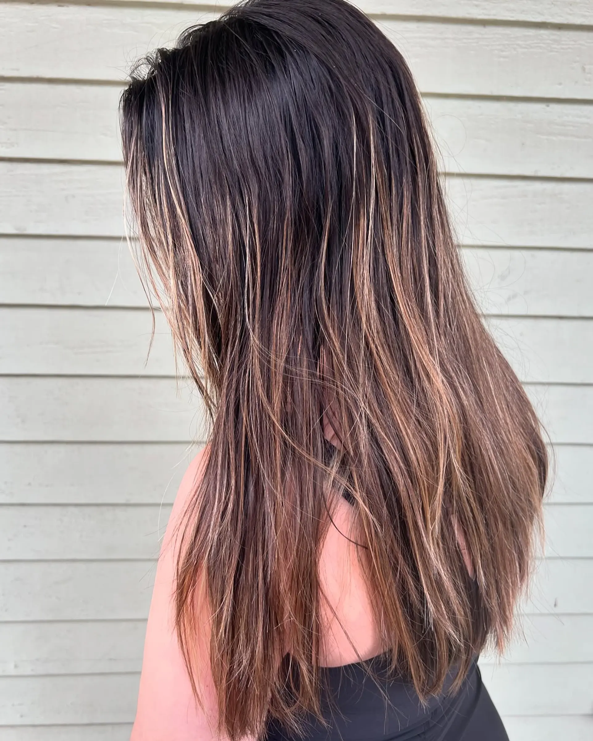 Long, straight hair styled with subtle layers and accentuated by warm caramel and golden-brown balayage highlights, offering a dimensional and sunkissed effect. 2
