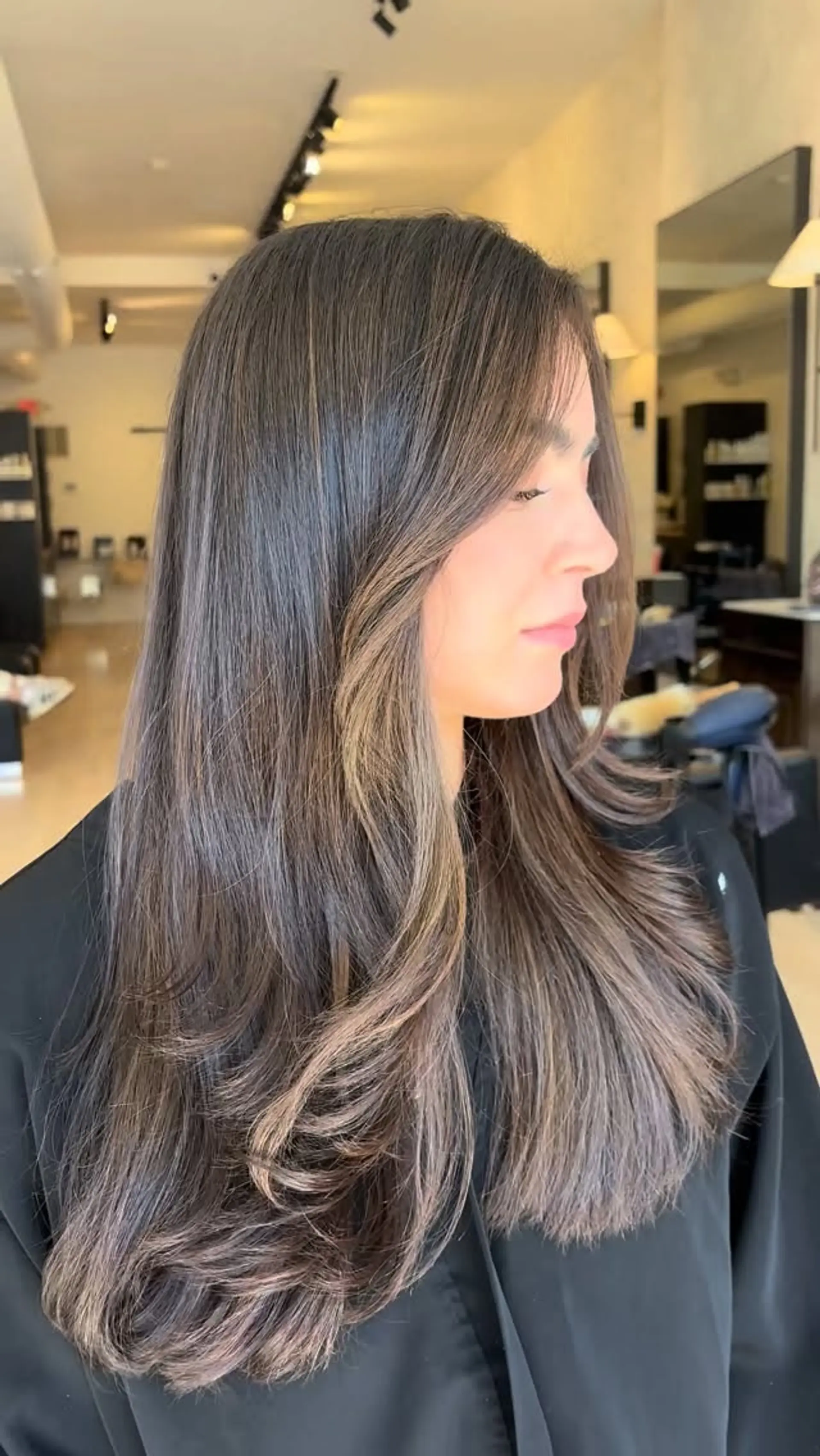 Long layered brunette hair with delicate sun-kissed face-framing highlights and a smooth, flipped blowout. 1