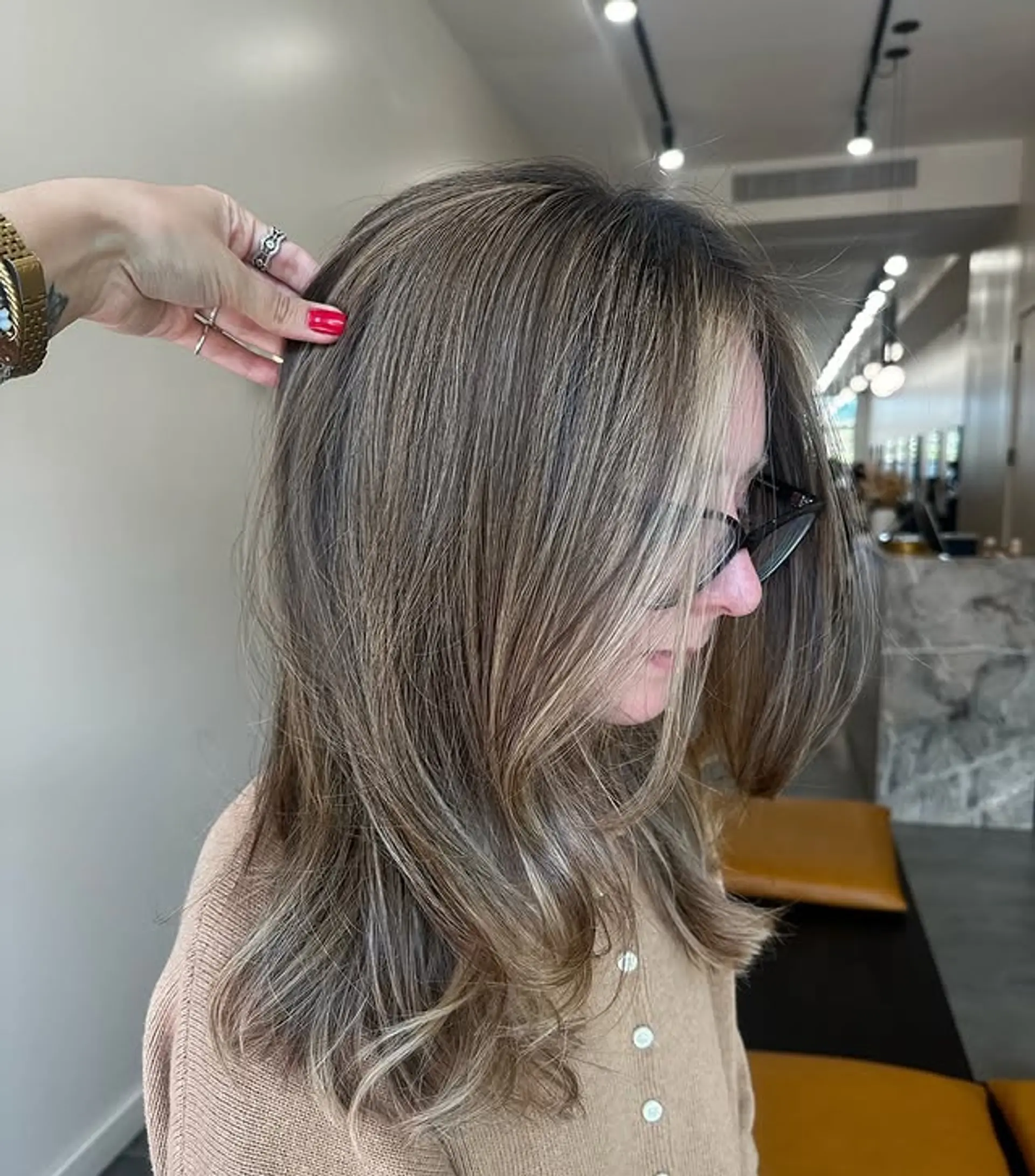 A medium-length layered hairstyle with a bronde balayage and face-framing layers. 1