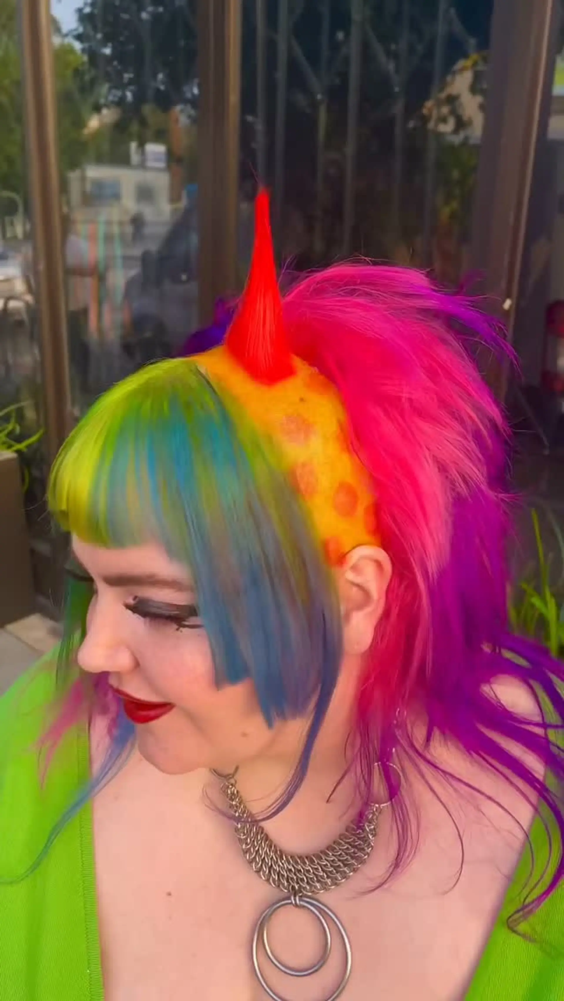A bold avant-garde clowncore punk style featuring a blunt green and blue fringe, shaved polka-dot section, sculpted red horn, and vivid pink and purple layers. 1