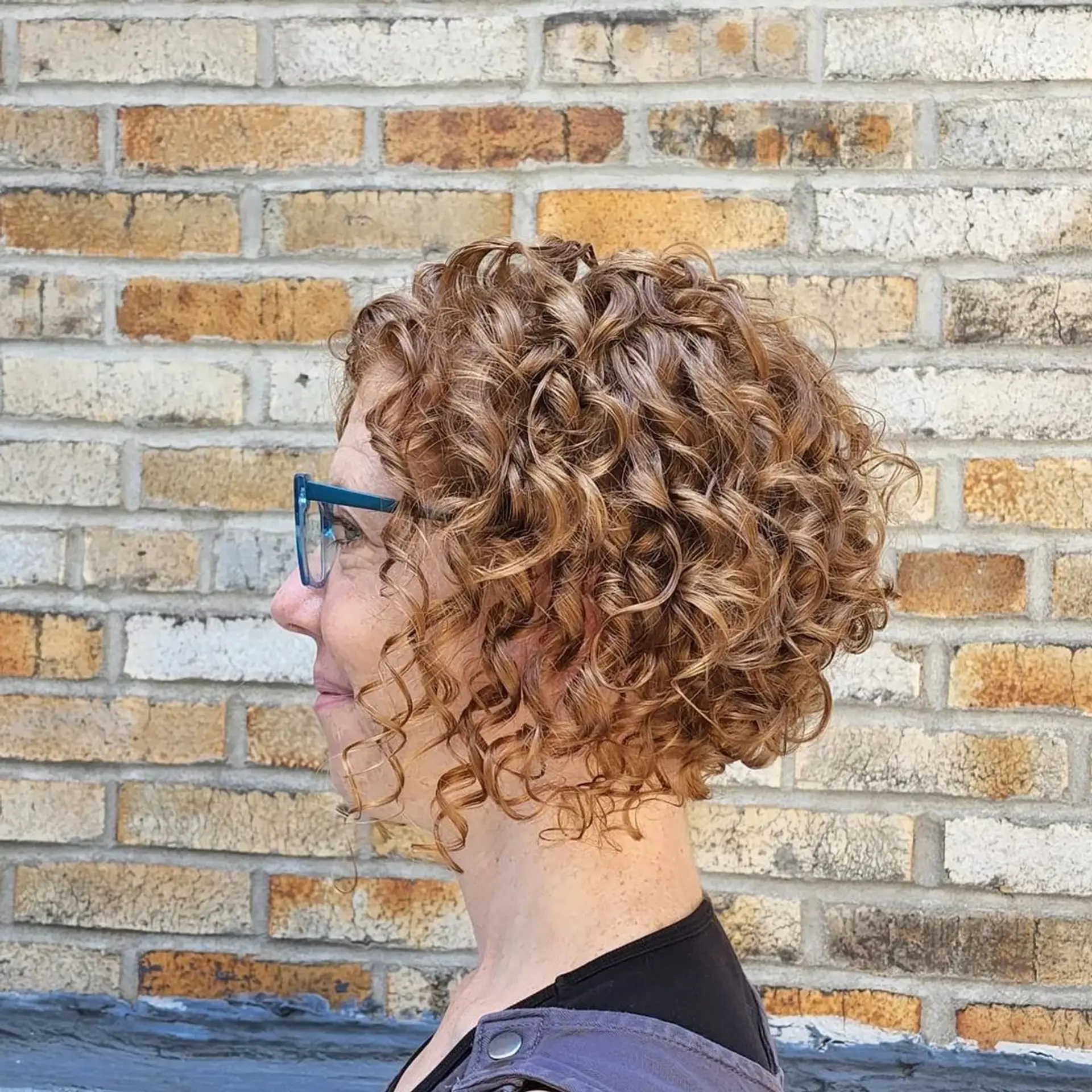 The Golden Spiral Bob features short, curly hair with tight, defined ringlets in a rich blend of golden brown and honey blonde hues, offering natural volume and a playful yet sophisticated layered cut. 2