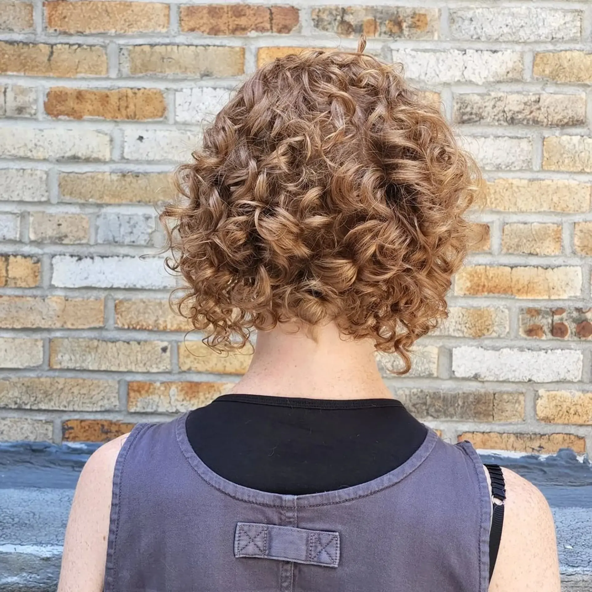 The Golden Spiral Bob features short, curly hair with tight, defined ringlets in a rich blend of golden brown and honey blonde hues, offering natural volume and a playful yet sophisticated layered cut. 3