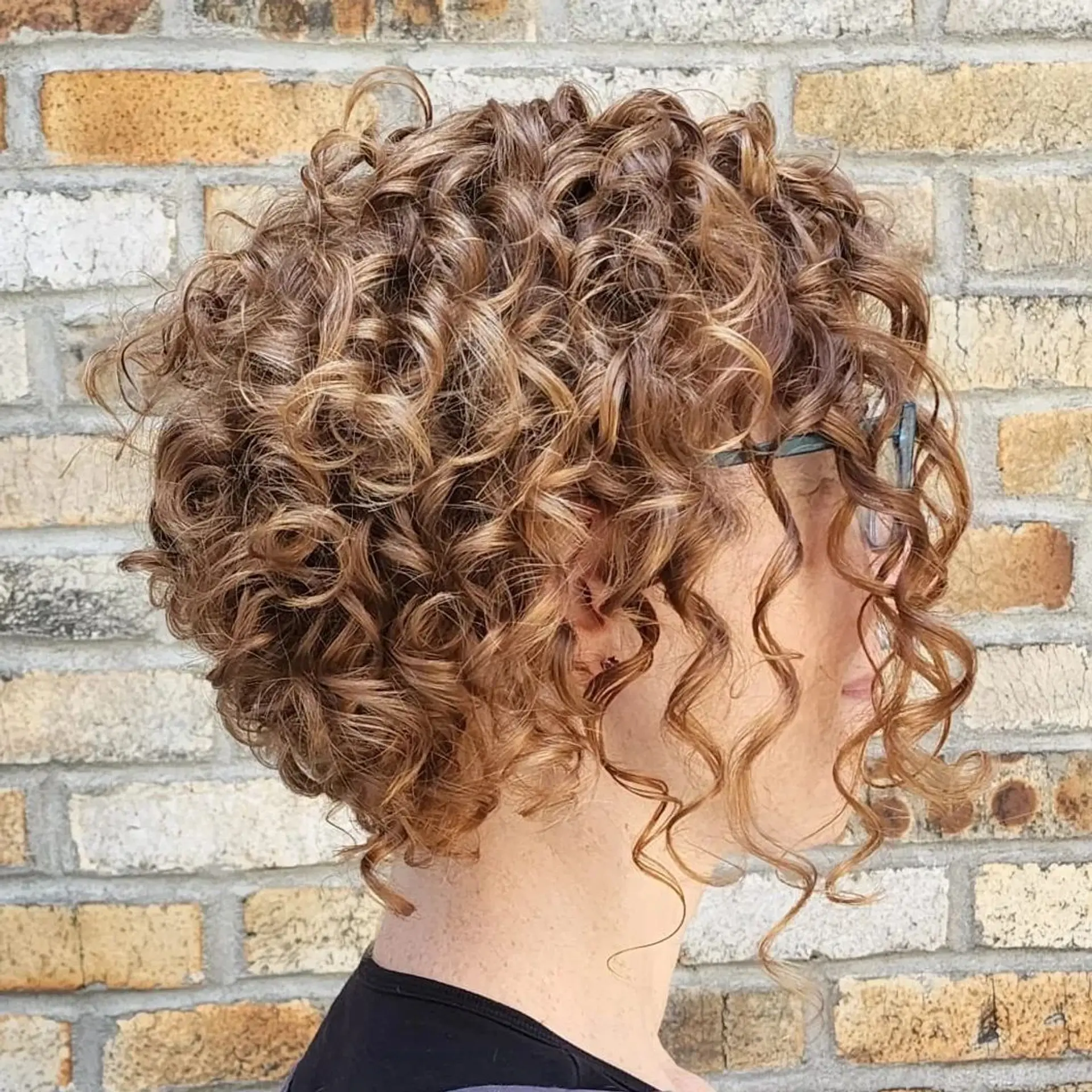 The Golden Spiral Bob features short, curly hair with tight, defined ringlets in a rich blend of golden brown and honey blonde hues, offering natural volume and a playful yet sophisticated layered cut. 1