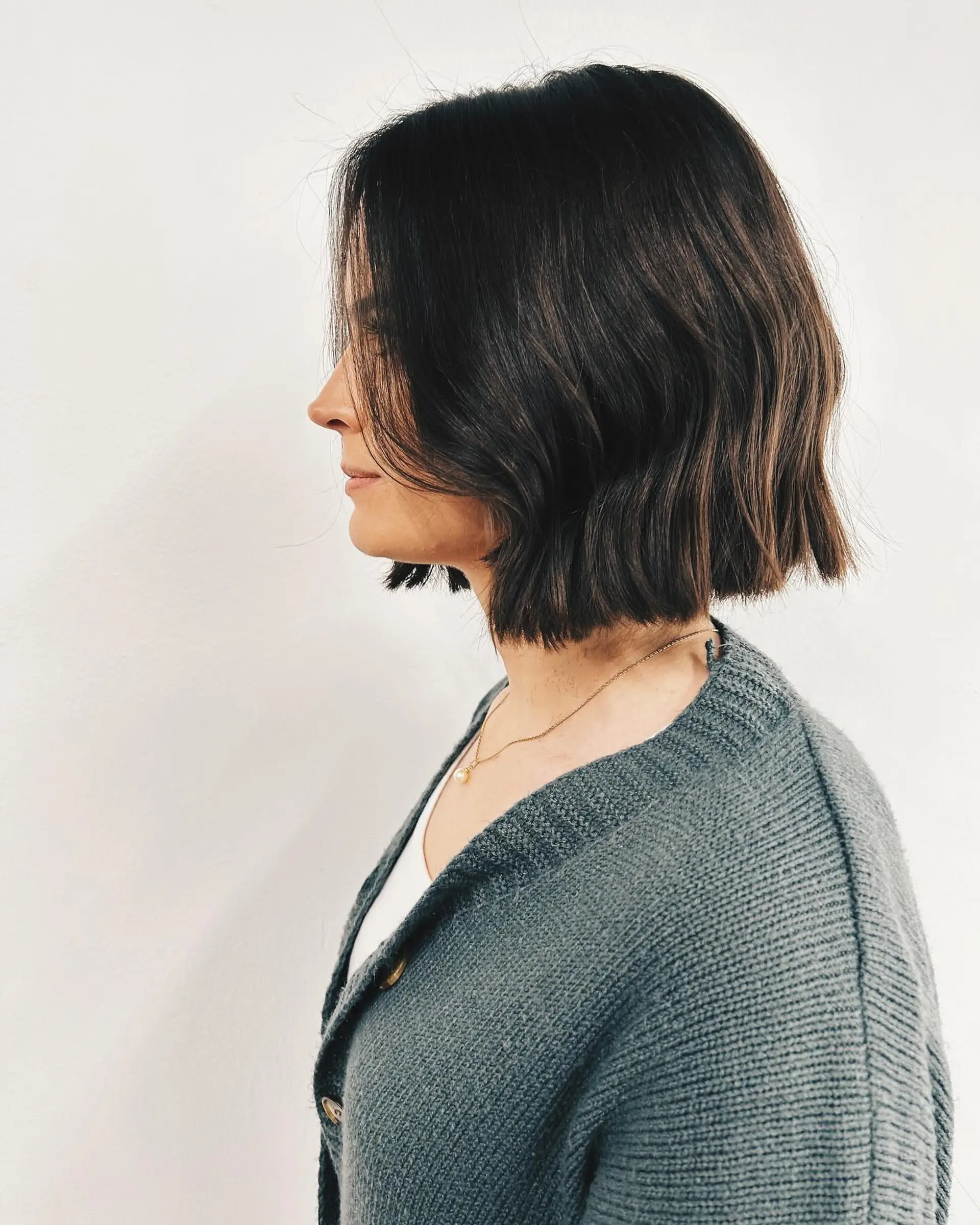 A chic, blunt bob cut to the jawline with subtle lived-in waves in a rich dark brunette tone. 1