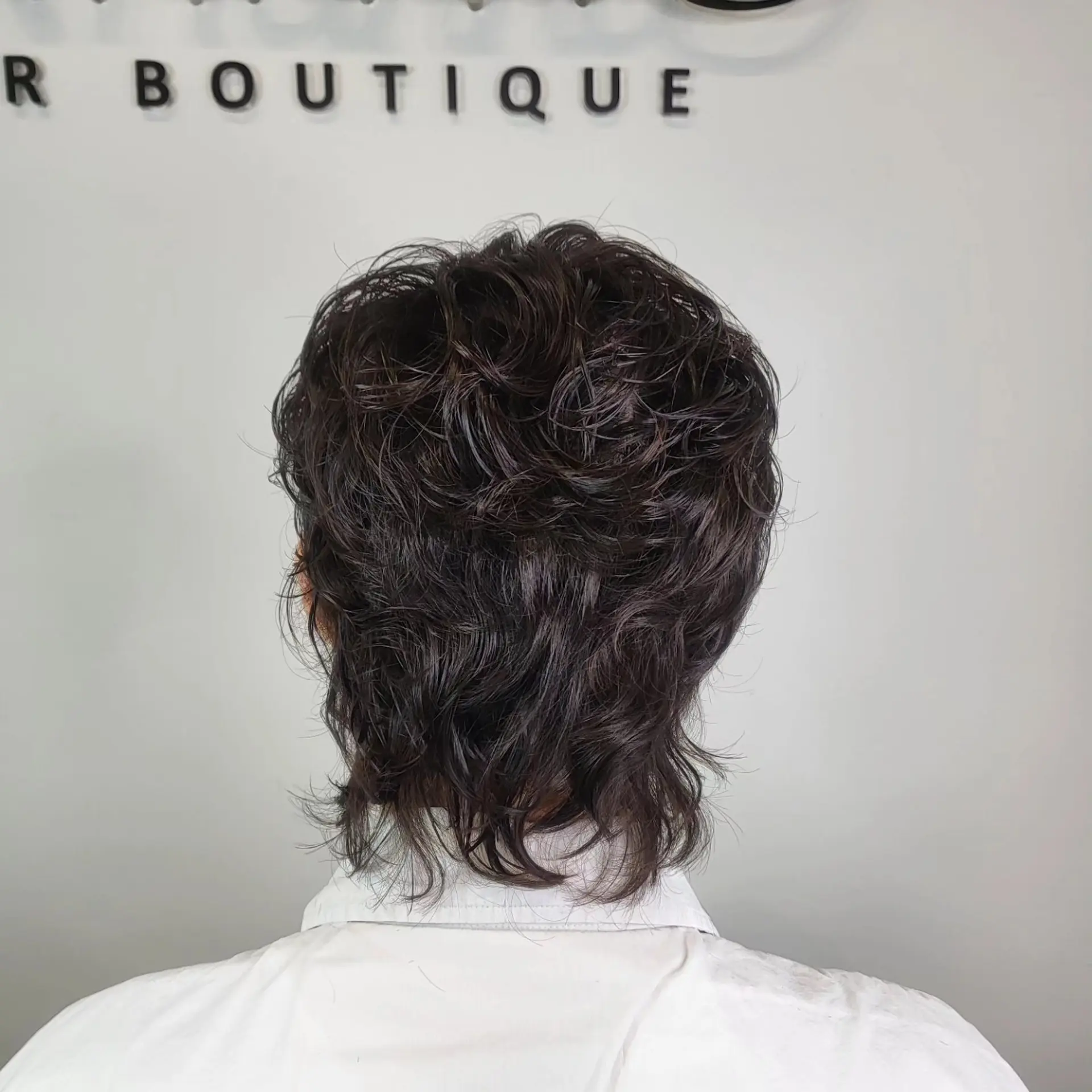 A layered, textured cut with defined waves and soft curls extending down the nape in a modern mullet silhouette. 1