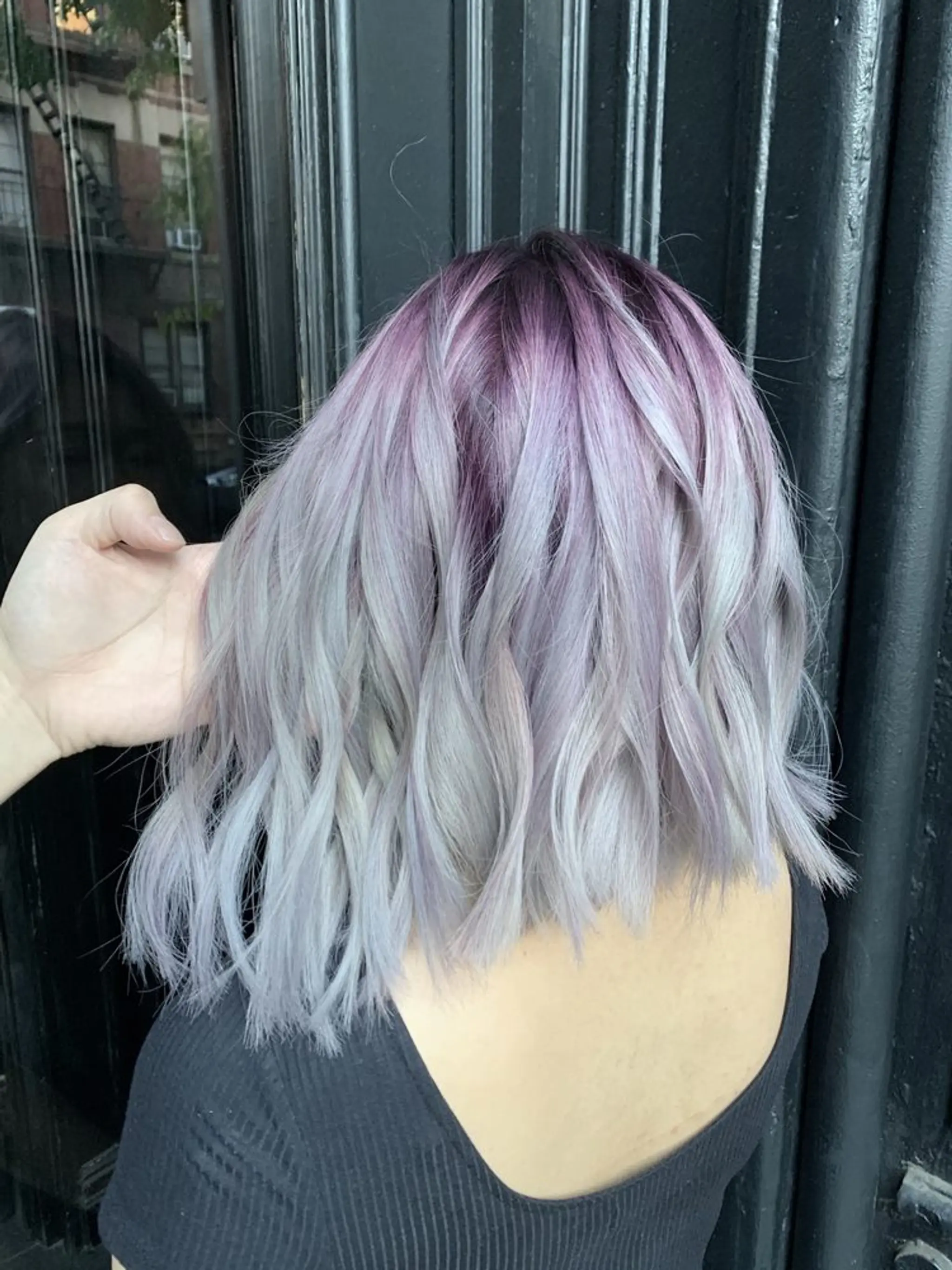 The hairstyle features a medium-length wavy bob with a stunning gradient of lilac, silver, and lavender hues. The waves add volume and texture, making the hair look lively and full. The cut is gently layered, giving it a soft, yet edgy finish.