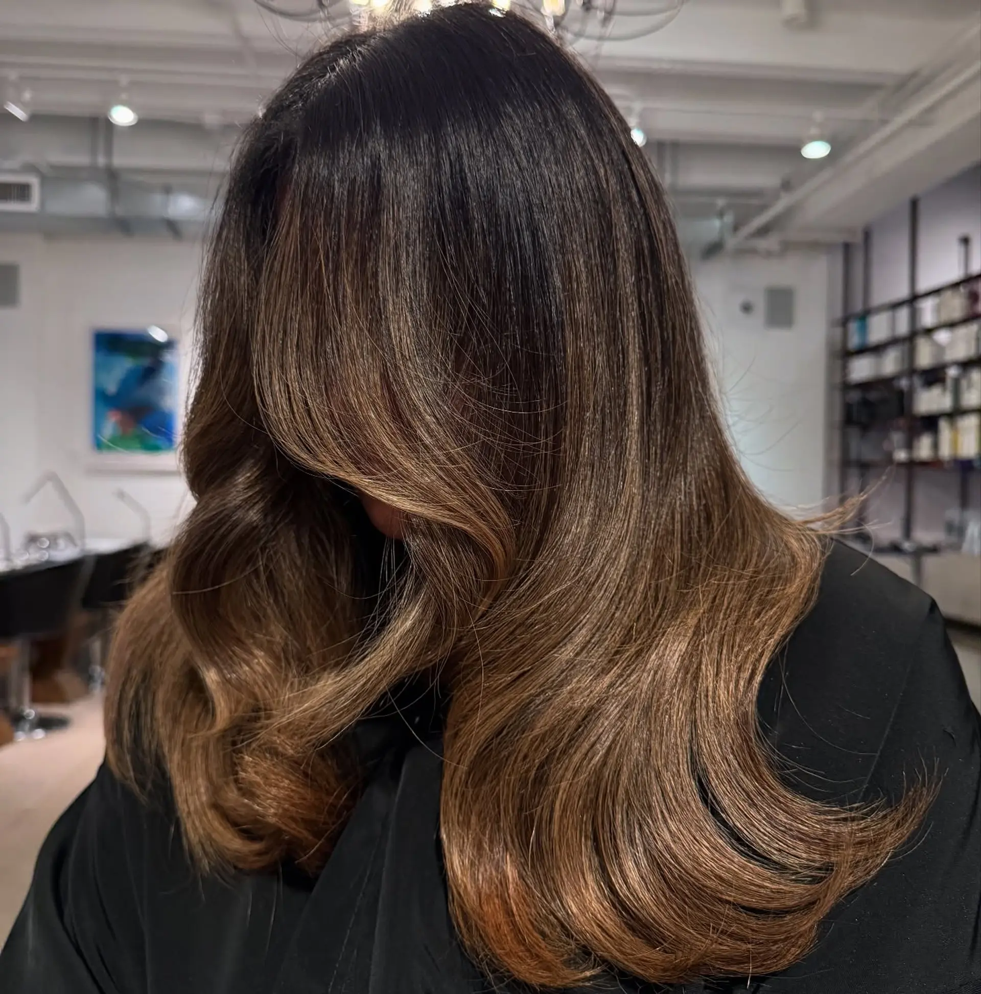 A rich dark brunette base transitioning into warm golden caramel balayage, finished with loose, voluminous waves. 1