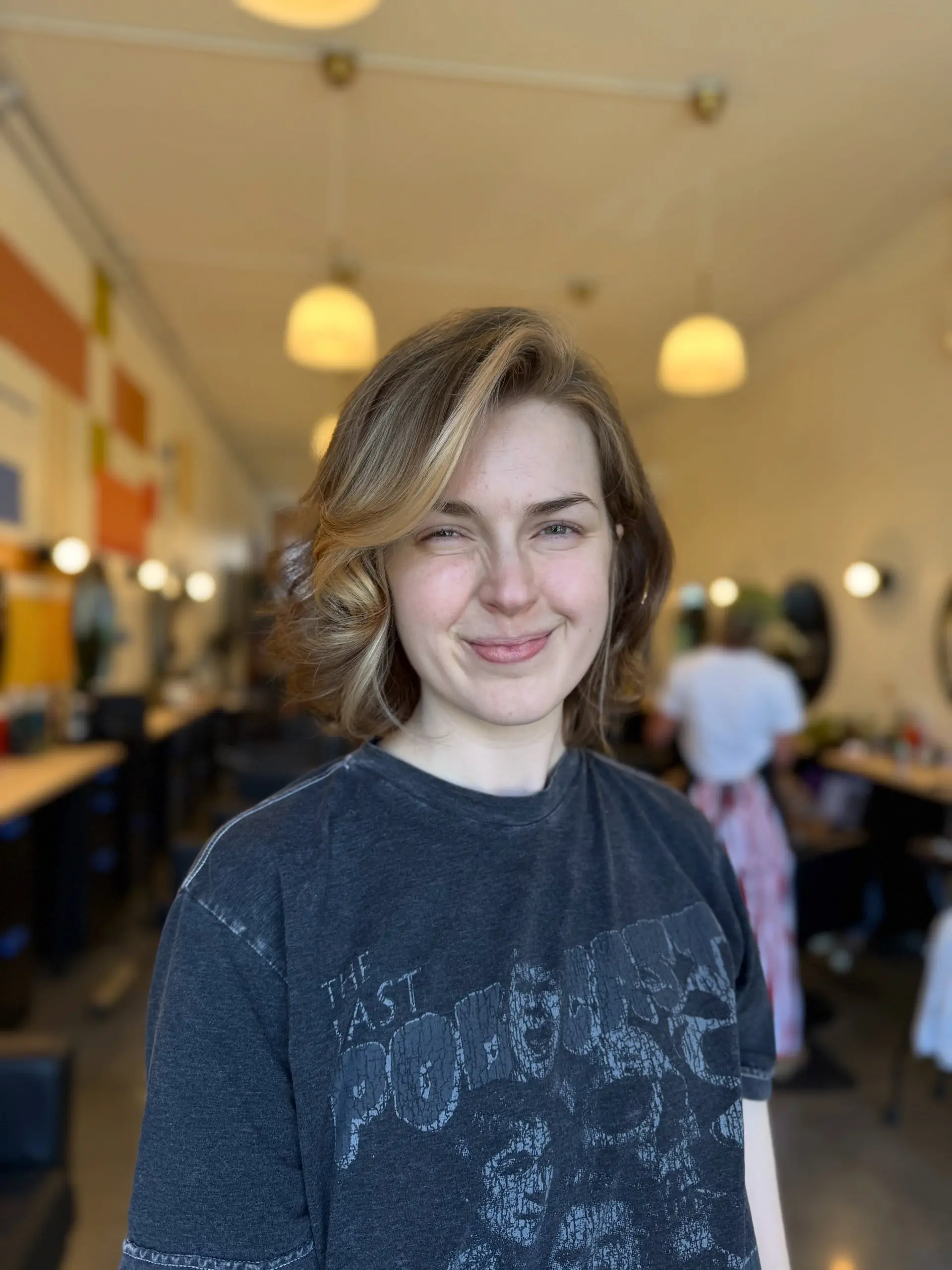 A chin-length layered bob styled with soft, voluminous side-swept waves and dimensional warm blonde highlights. 1
