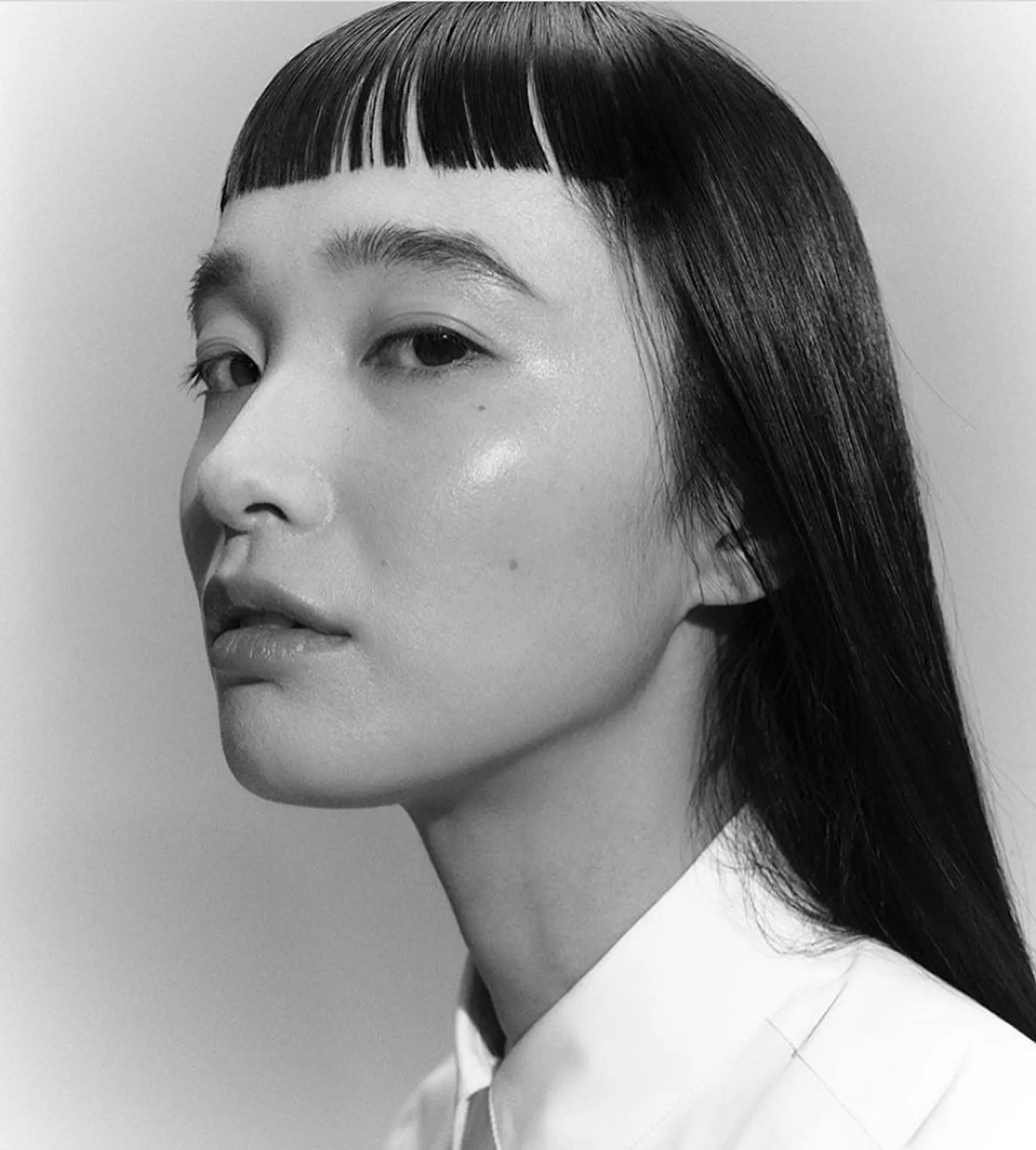 A long, sleek, and straight hairstyle with jet-black hair. It features precision-cut blunt bangs offering a contemporary, sophisticated appeal.