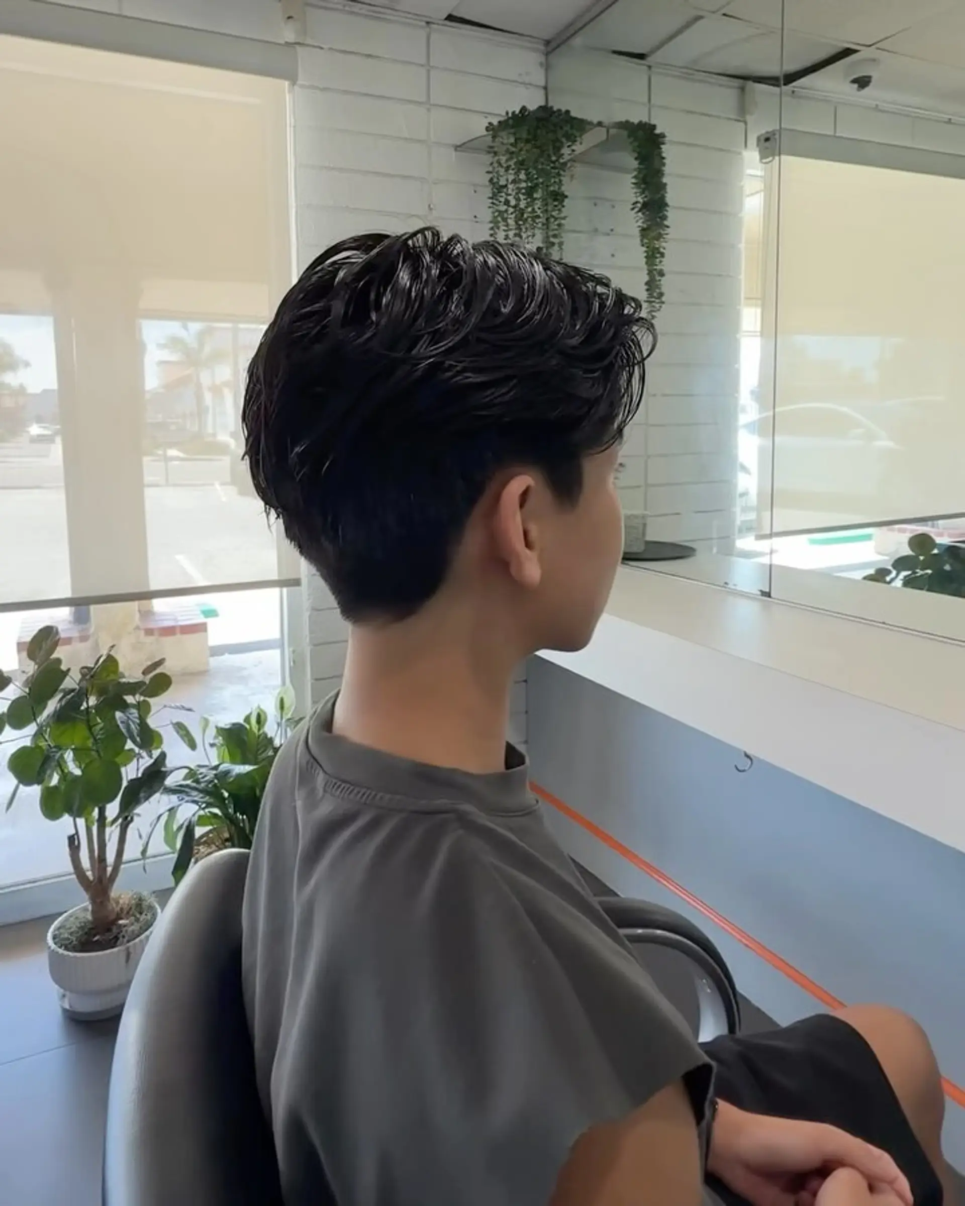 A short men's cut styled with a soft textured wave perm flowing smoothly back from the face with a tapered nape. 1