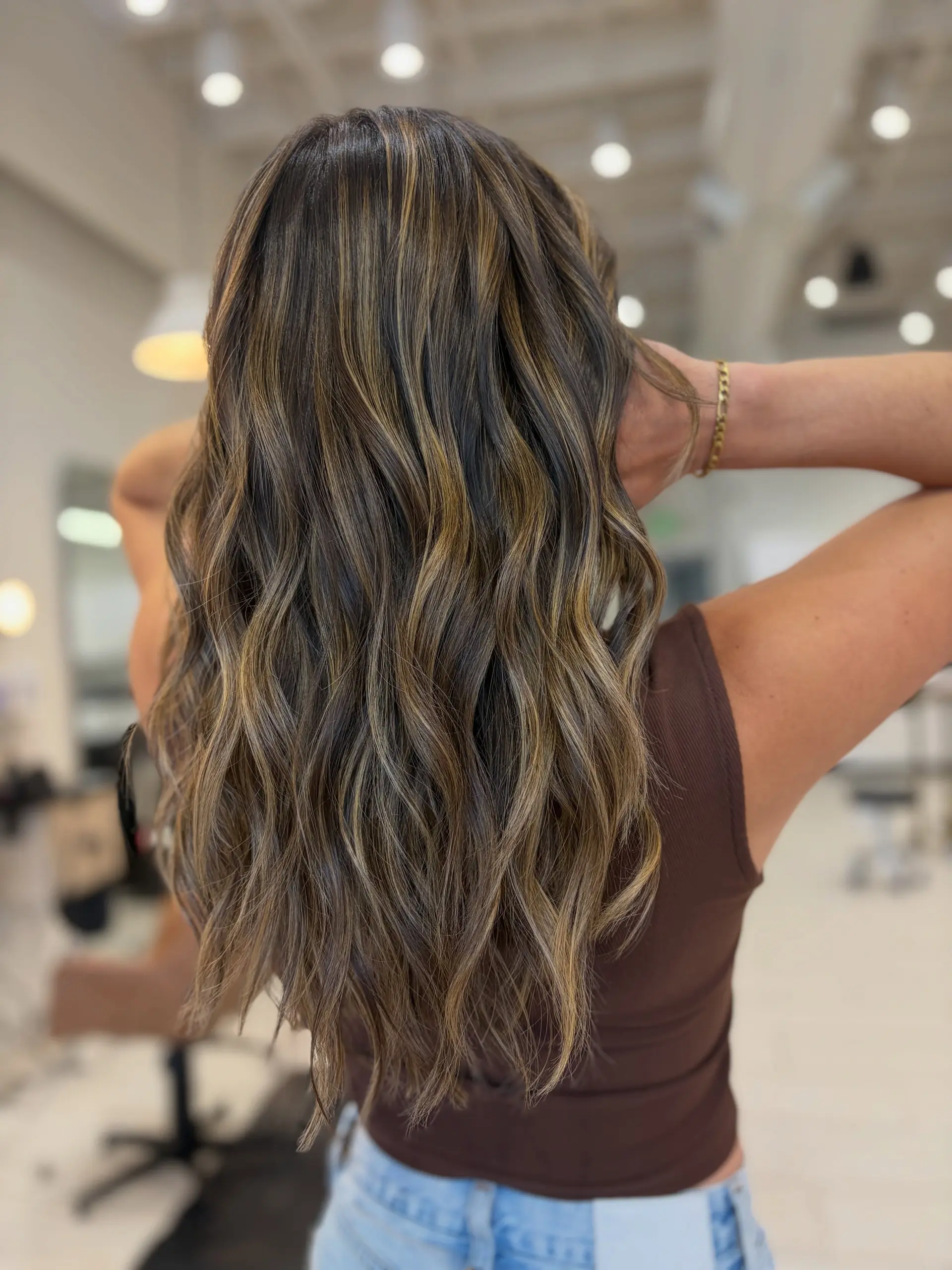 Long dimensional brunette hair styled in loose, textured waves with warm caramel highlights. 1