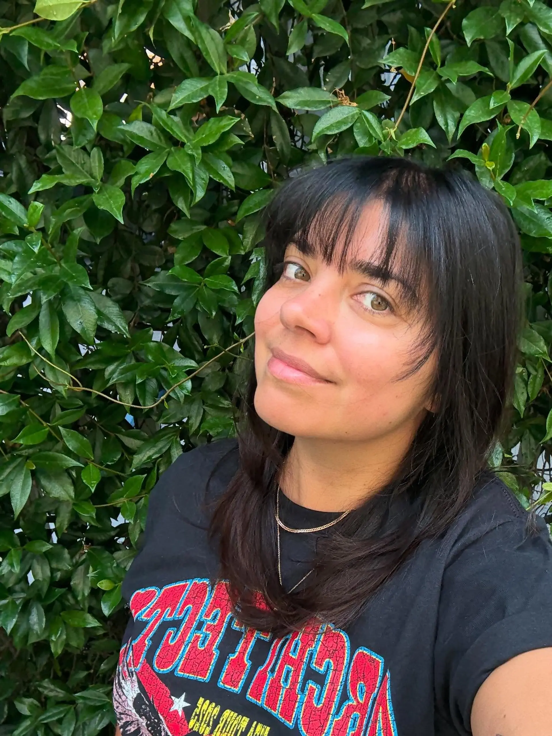 Medium-length dark haircut featuring soft, face-framing layers and wispy straight-across bangs. 1