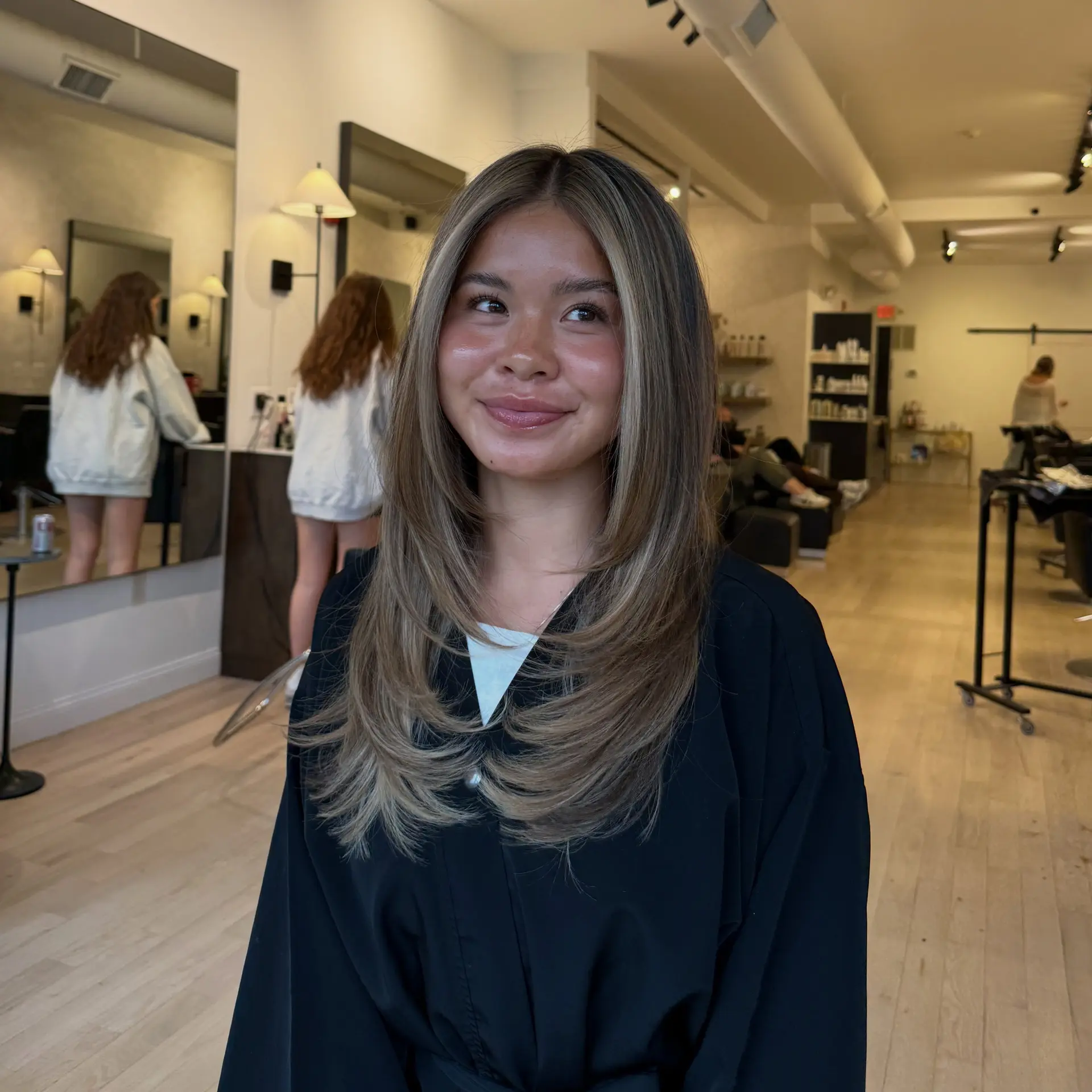 Long layered cut styled with bouncy, inward-curling face-framing layers and dimensional bronde highlights. 1