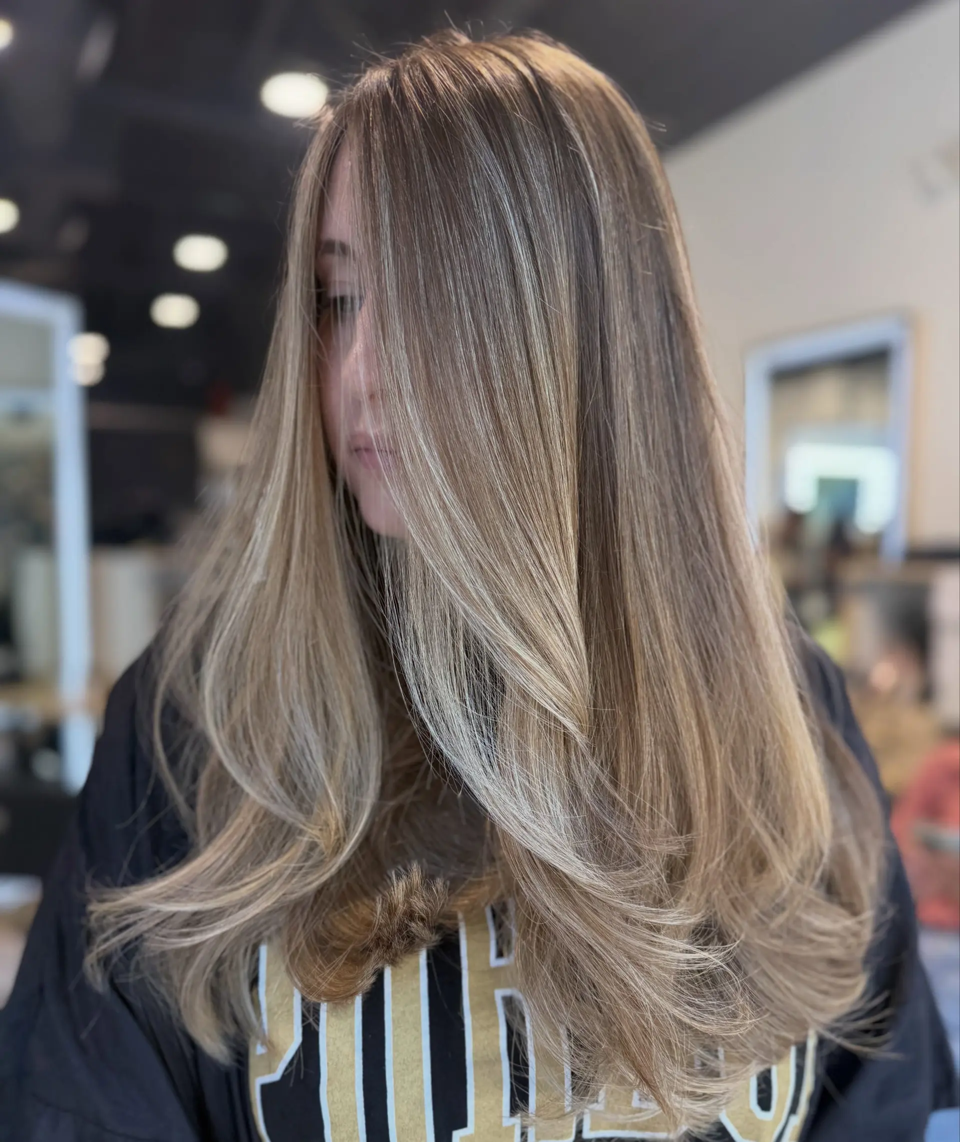 Long dimensional light brown hair enhanced with fine blonde babylights, shaped with long layers and styled into a voluminous, smooth blowout. 1