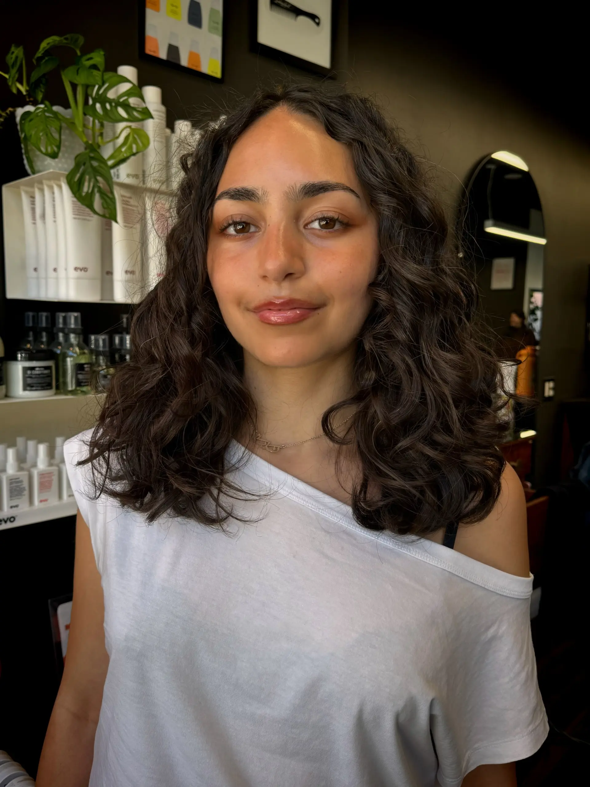 A mid-length layered cut styled with defined, bouncy dark brown waves and curls parted down the middle. 1