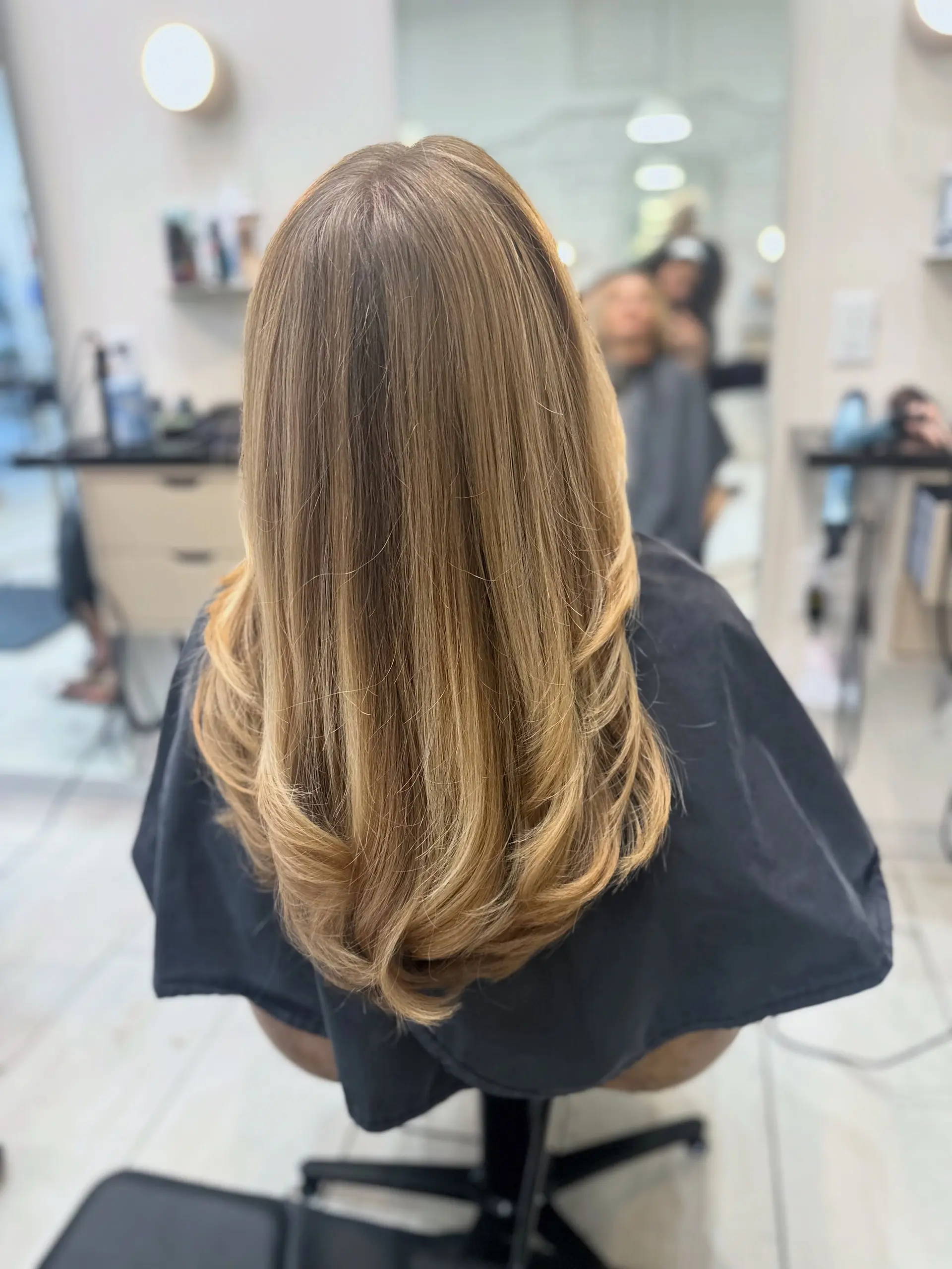 Long honey blonde hair cut with flowing layers and styled with soft, curled-under ends. 1