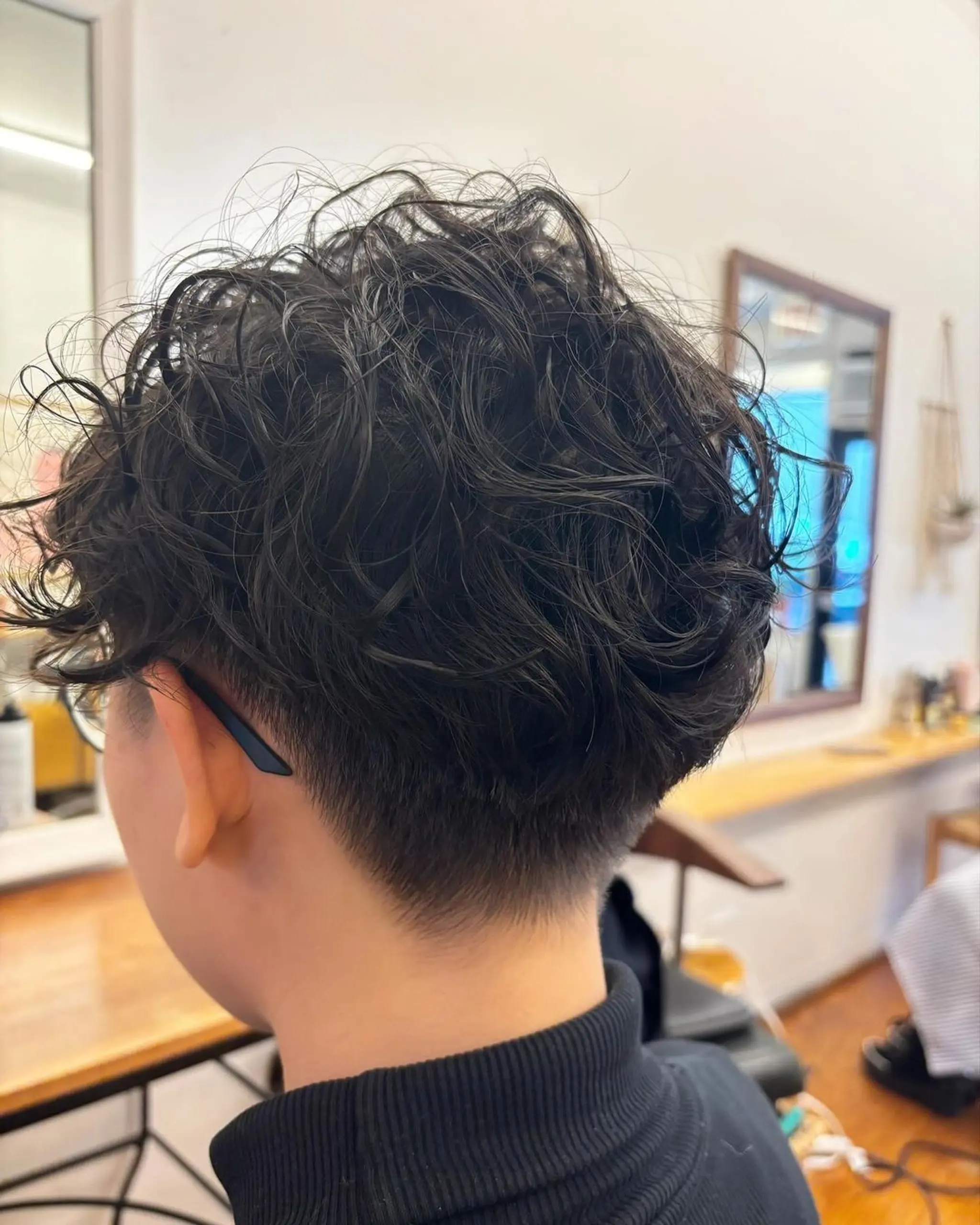 This hairstyle features a cool curly top with natural volume, tapering into a neat undercut at the sides and back. 2