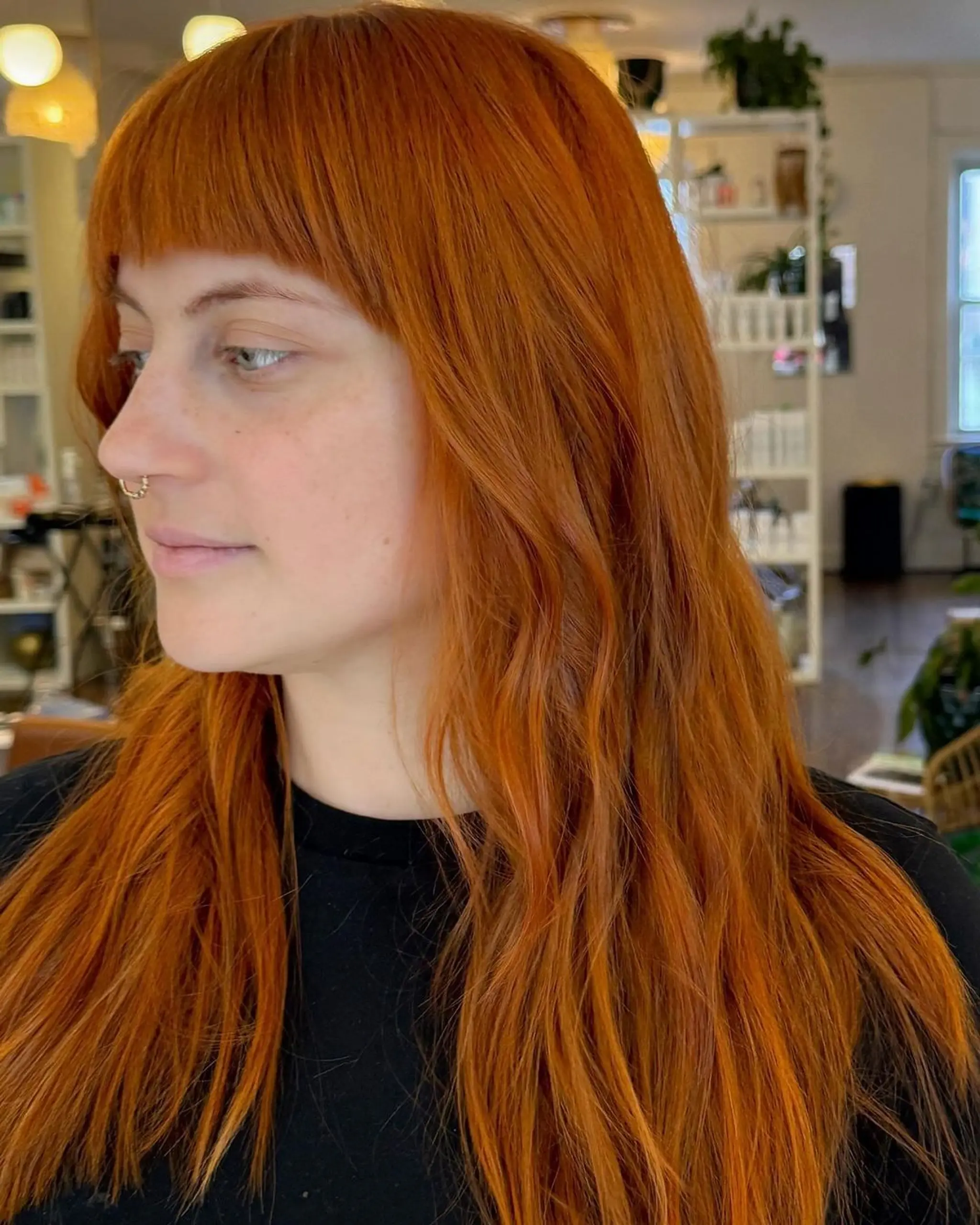 A long, wavy style with copper color featuring blunt bangs and soft, cascading waves that give a vibrant effect.