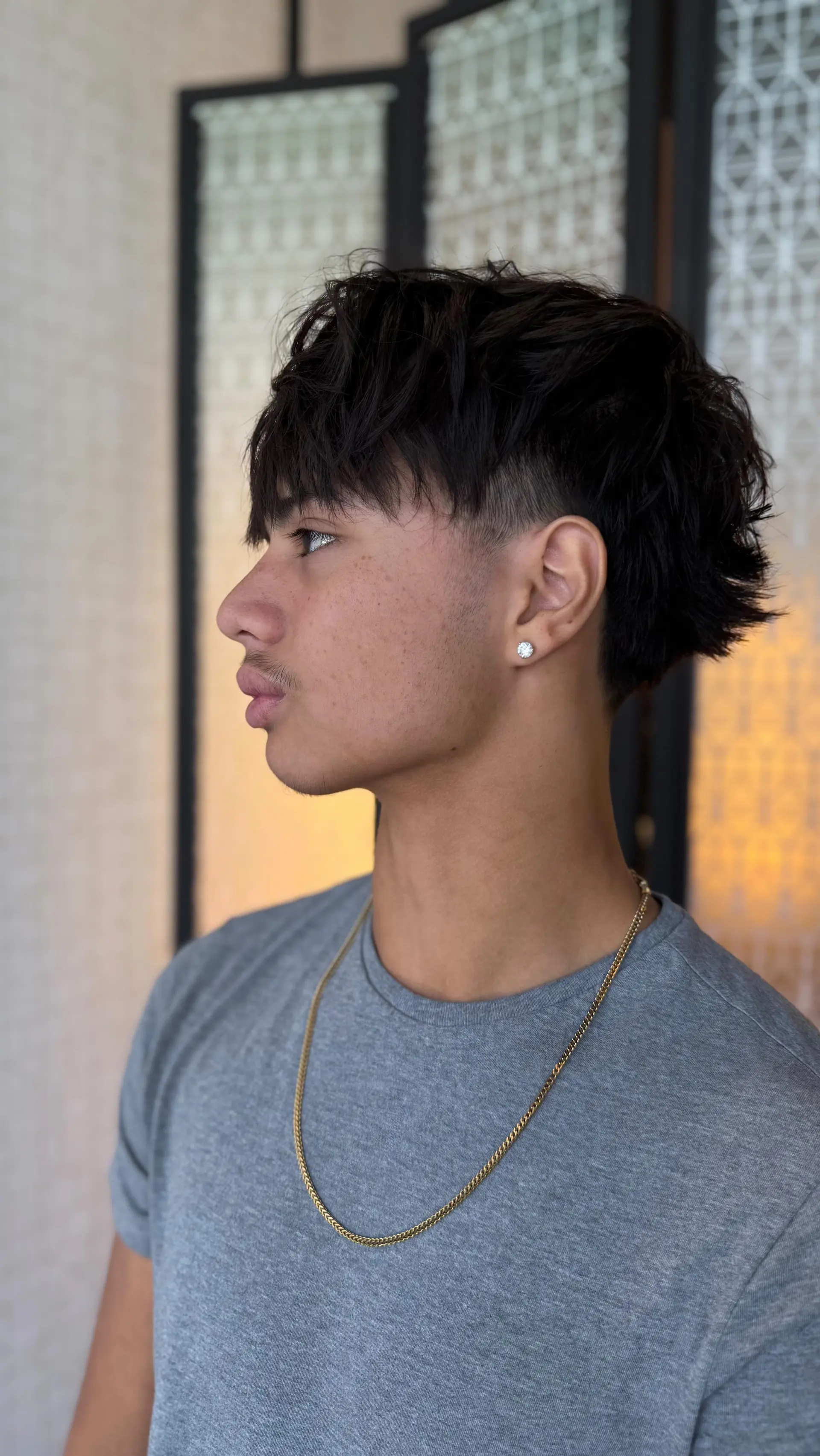 A modern textured mullet featuring a clean temple taper fade, fringe bangs, and textured layers throughout the top and back. 1