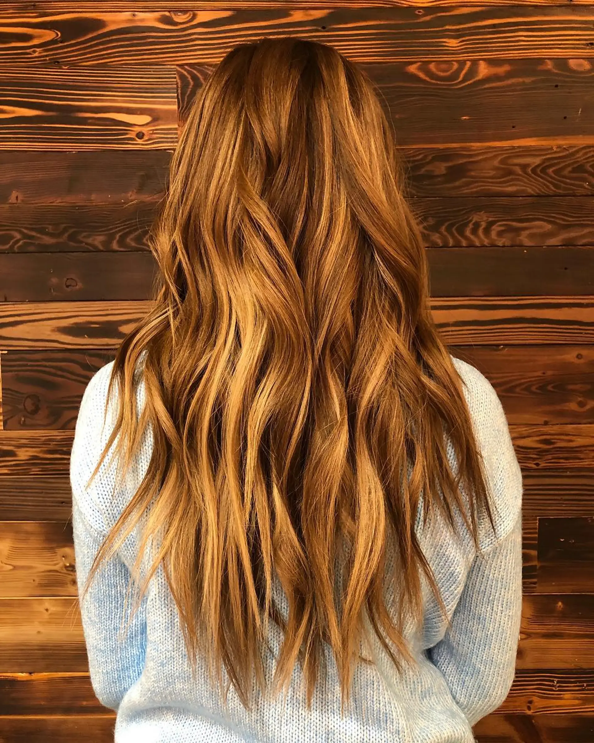 Long, wavy hair with a copper balayage, featuring a seamless blend of warm blonde and copper tones for added dimension. 1
