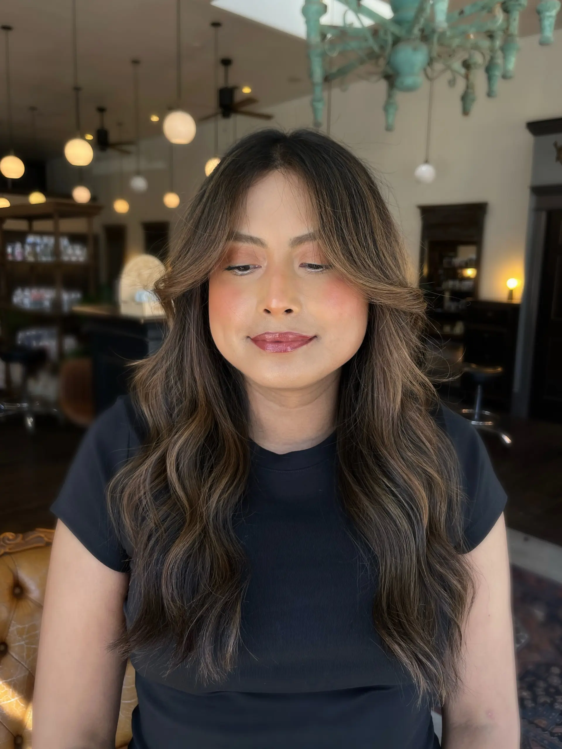 Long dimensional bronde hair featuring soft curtain bangs and styled loose, voluminous waves. 1