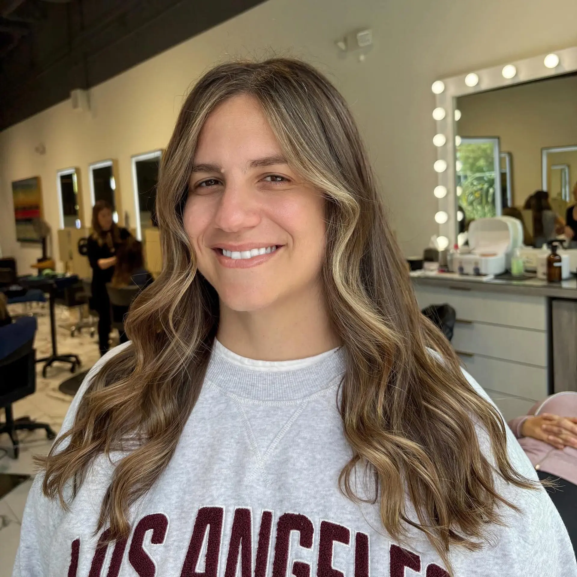Long dimensional bronde hair styled into soft loose waves with subtle face-framing highlights. 1