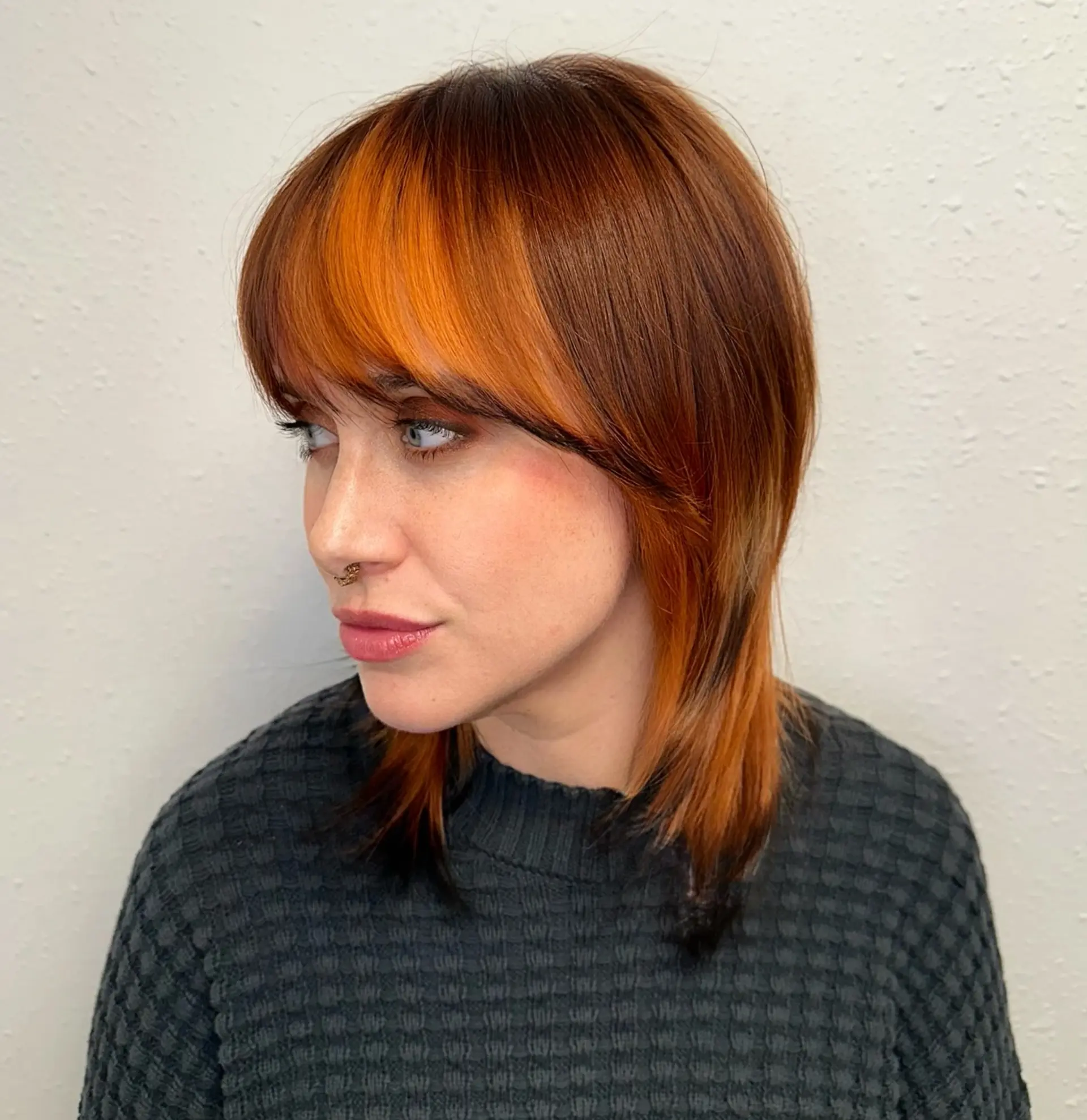 A medium-length layered shag haircut featuring warm copper tones with dark dimensional accents and full bangs. 1