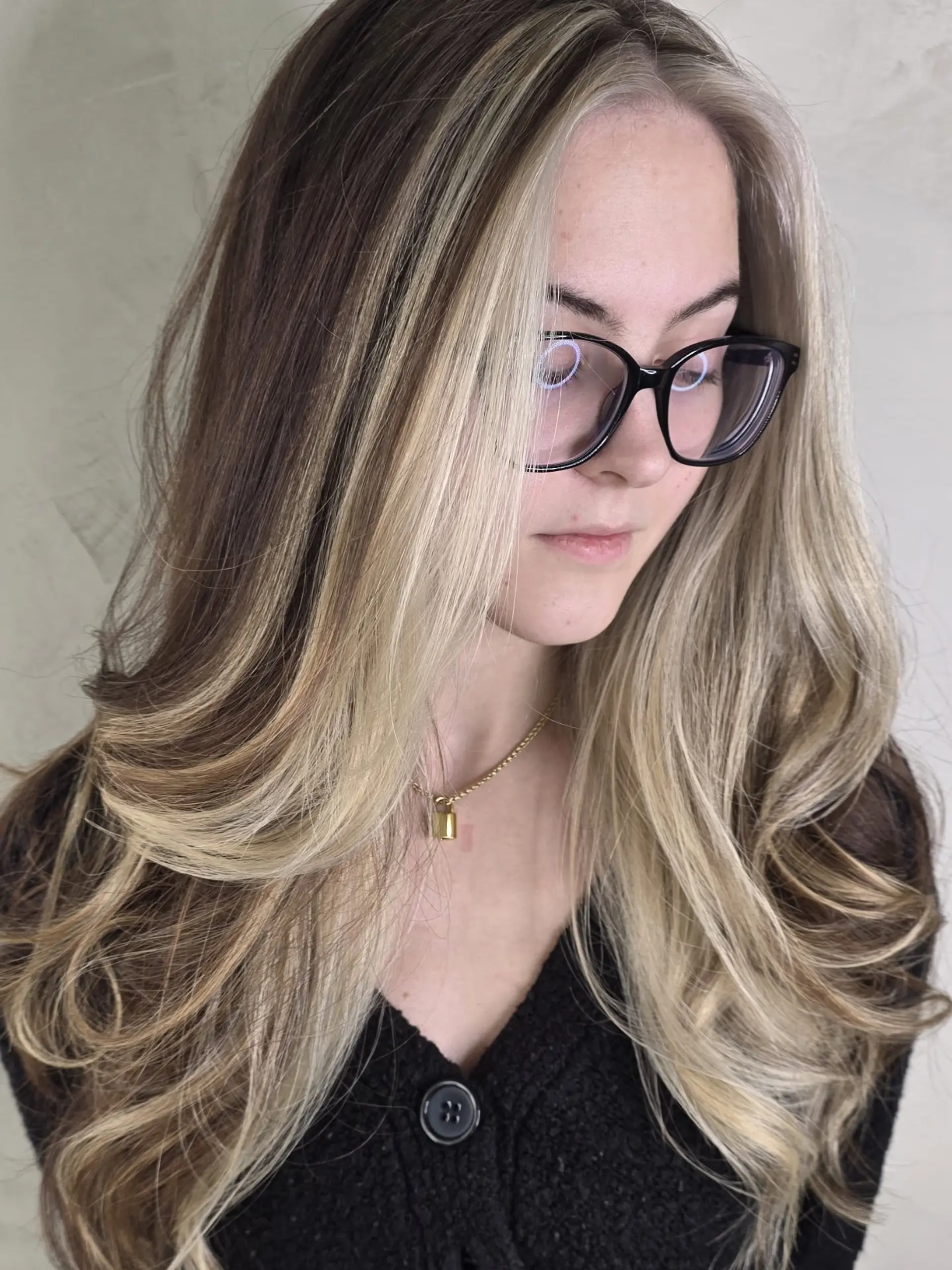 Long dimensional brunette hair styled with face-framing halo blonde highlights and soft outward waves. 1