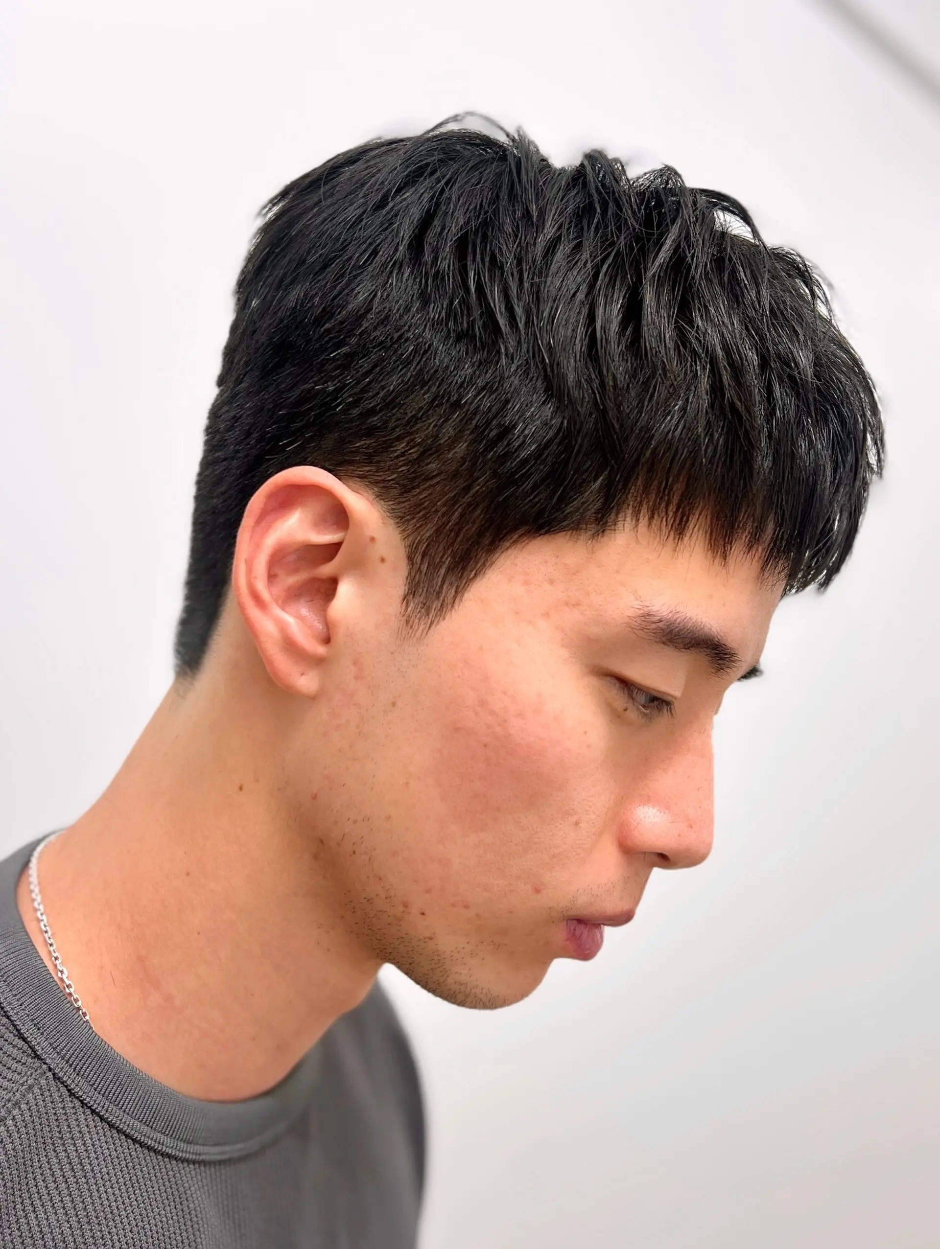 A modern short men's haircut with a sleek side down perm and a textured, piecey top with a short fringe. 1
