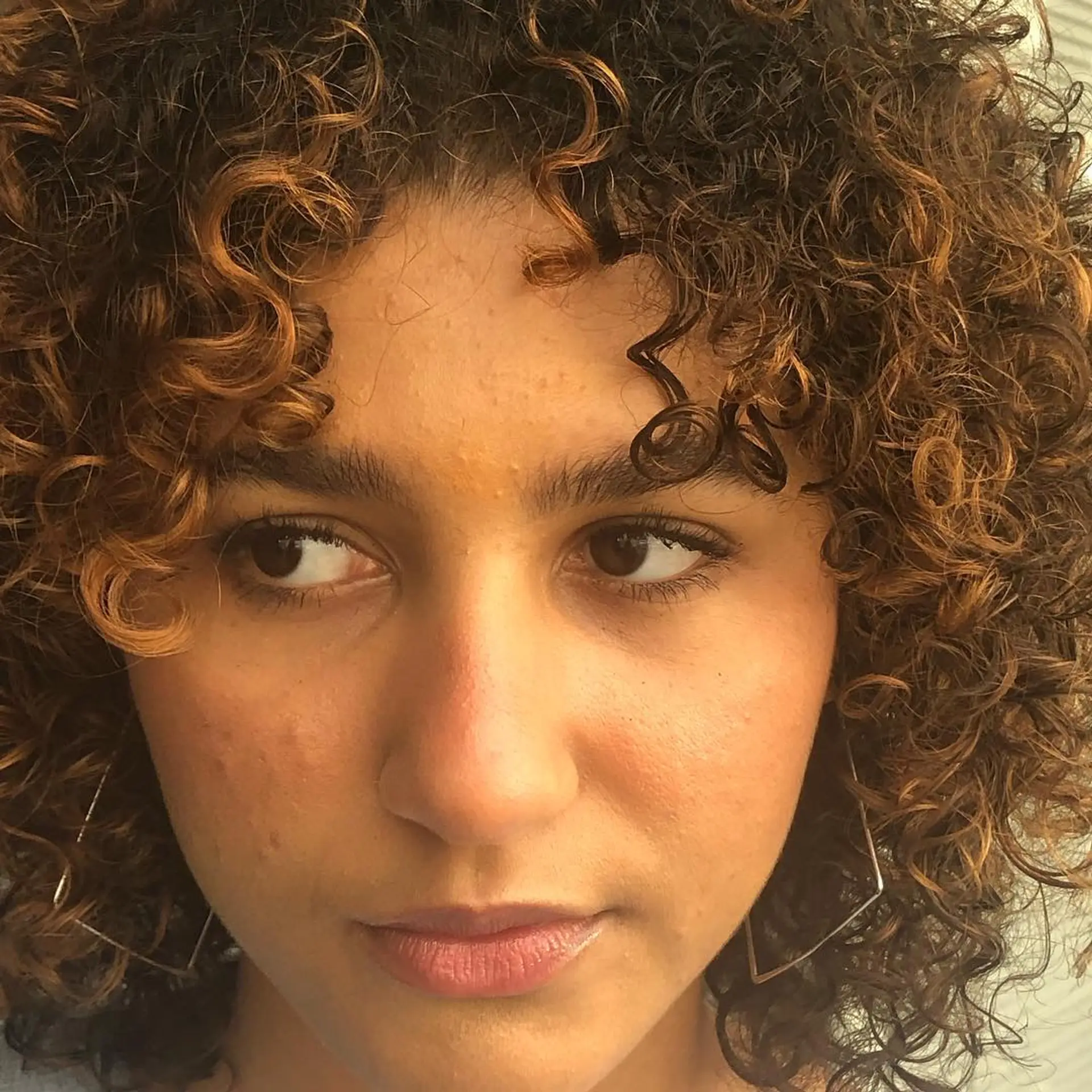 A textured dry cut on defined natural curls featuring soft face-framing fringe and warm caramel highlights. 1