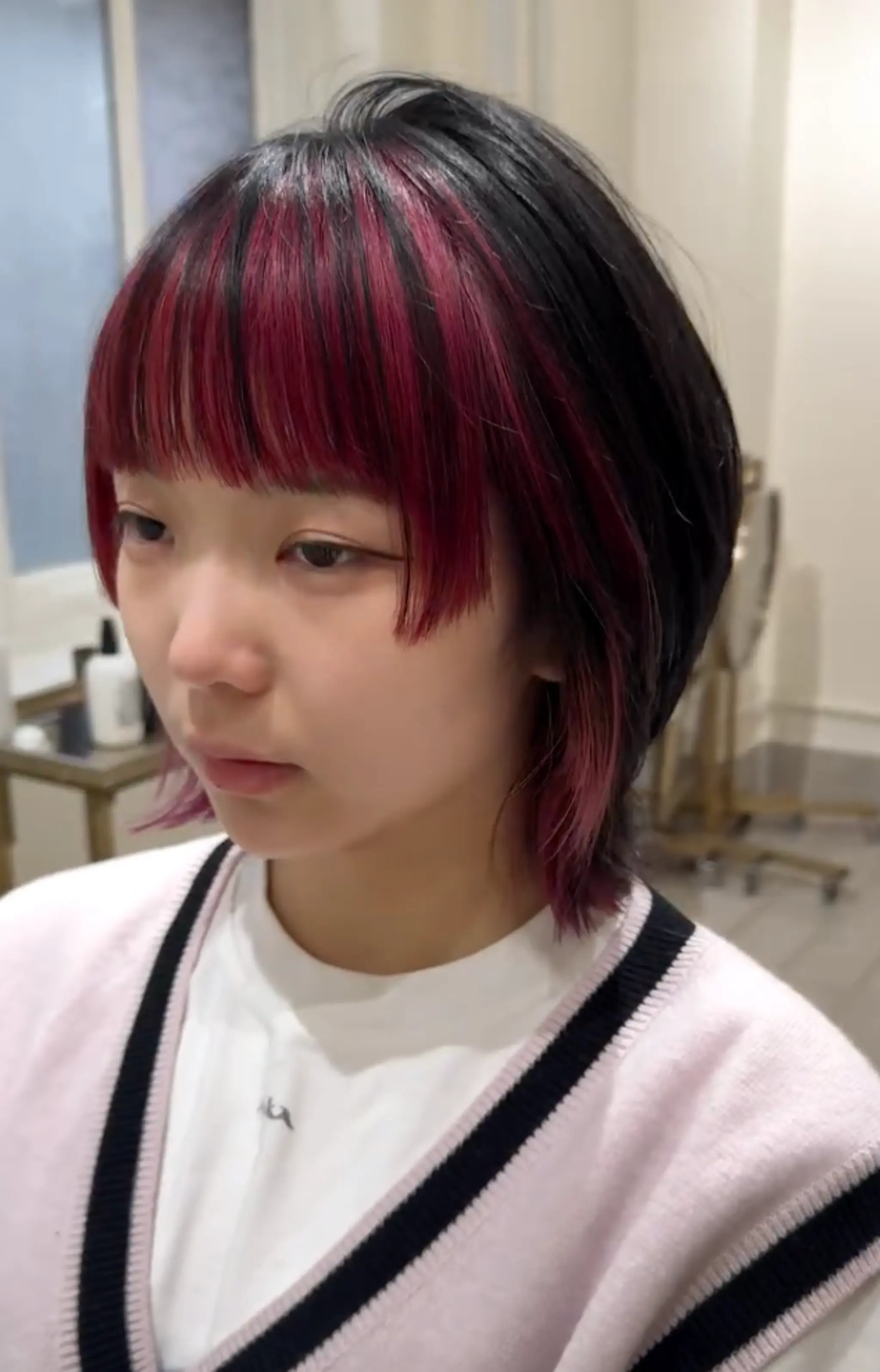 A medium-length, dual-tone hairstyle with black and magenta colors, featuring choppy layers and a fringe that frames the face in an edgy and modern look.