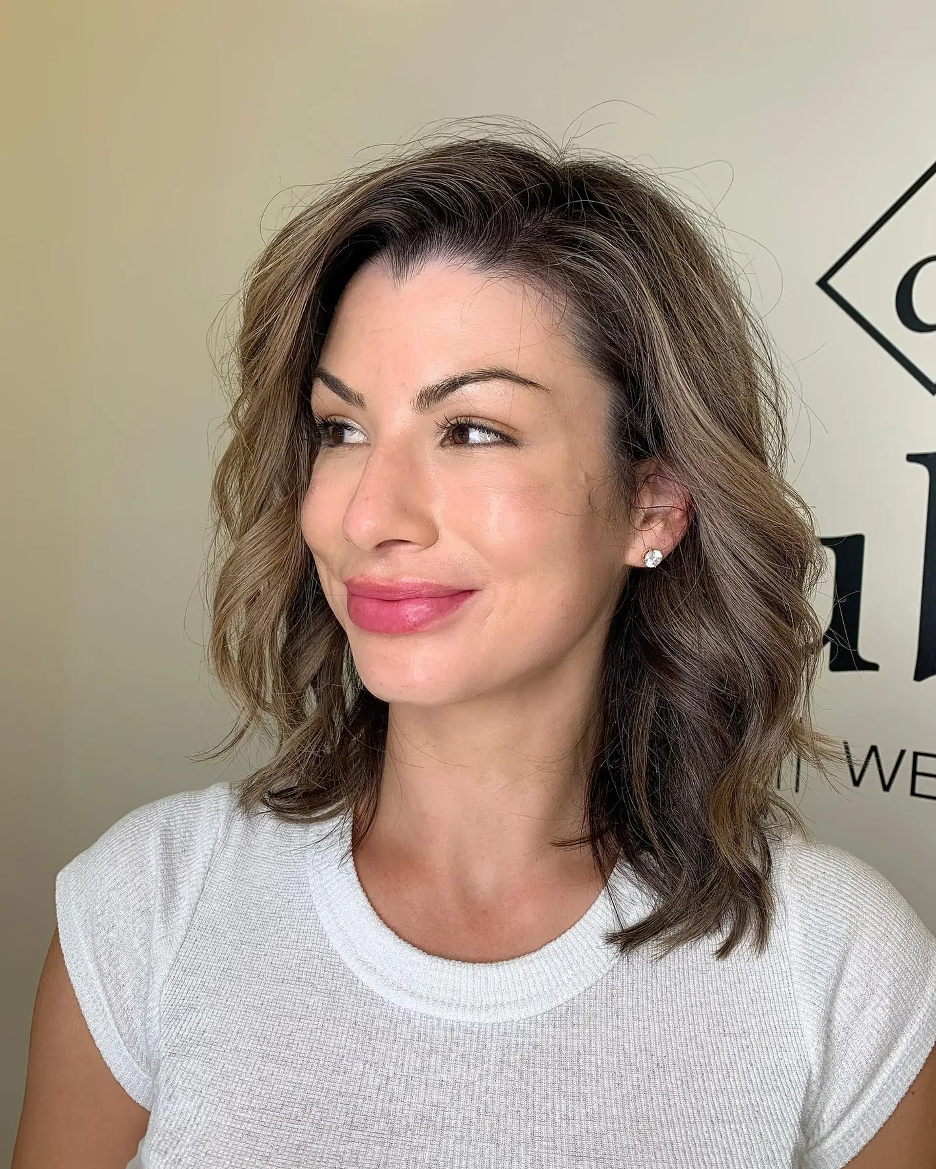 A textured collarbone-length lob styled in soft, undone waves with a side-swept part, featuring cool ash brown tones and seamless dimensional highlights. 1