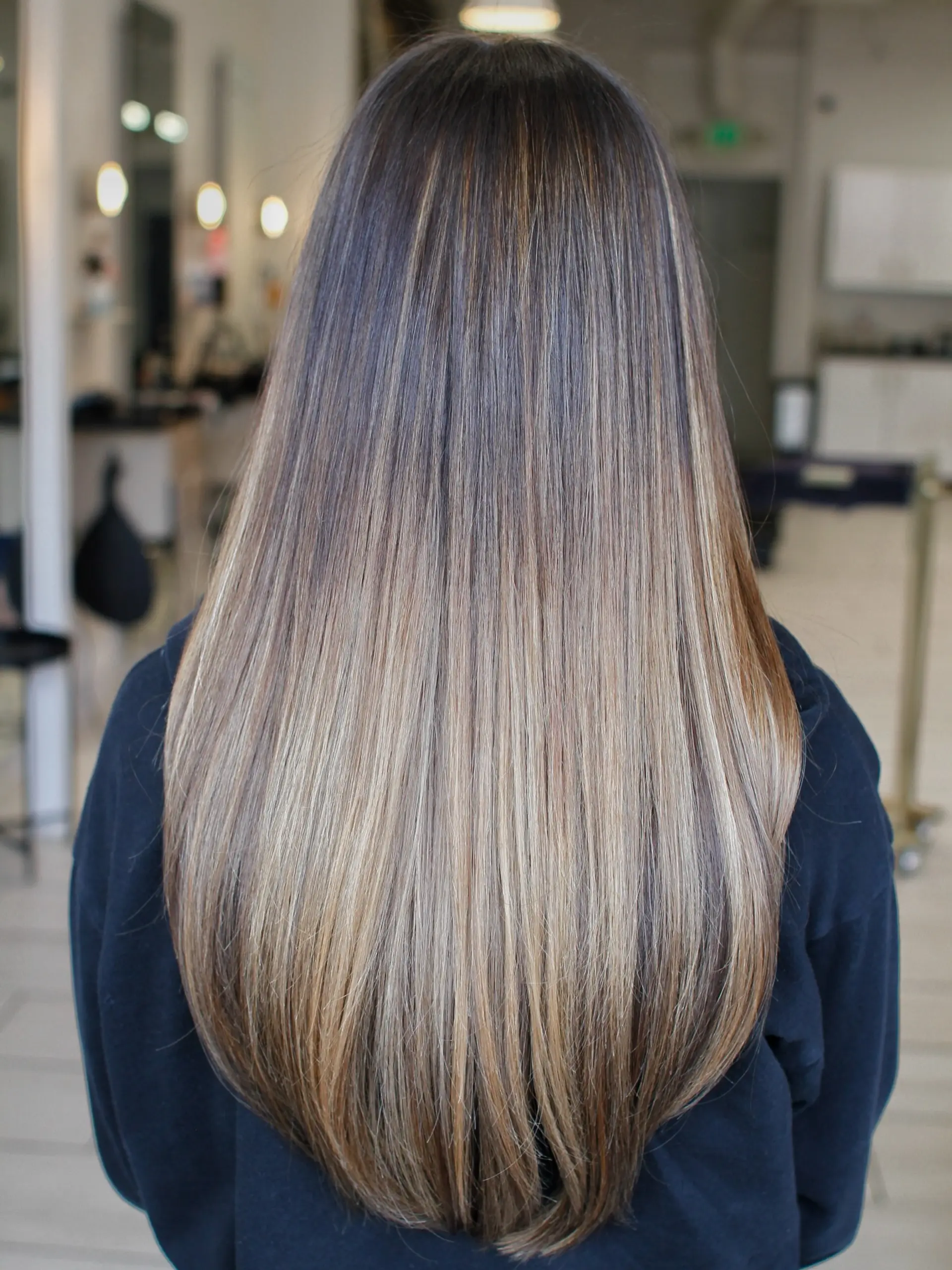 Long, silky straight brunette hair featuring fine, seamless multi-dimensional highlights blending into brightened ends. 1