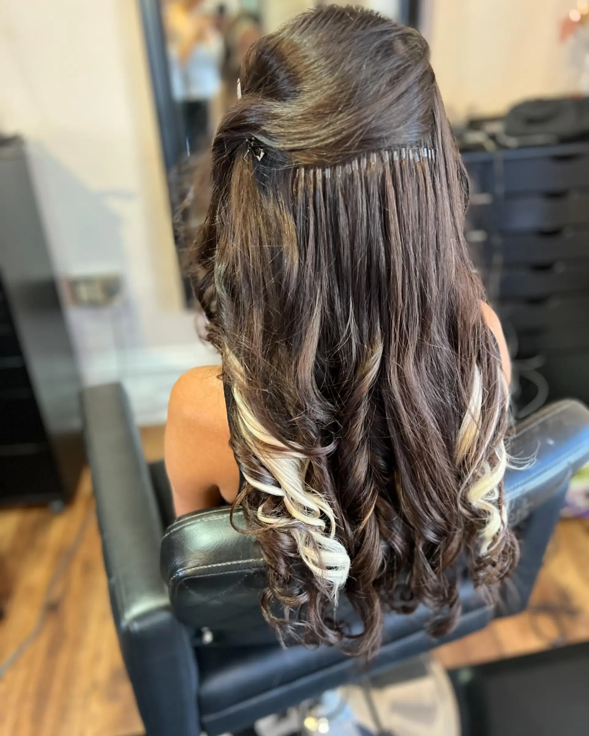 Long dark brown hair with blonde highlights styled in soft curls, with the top section pinned to showcase a clean microlink extension row. 1