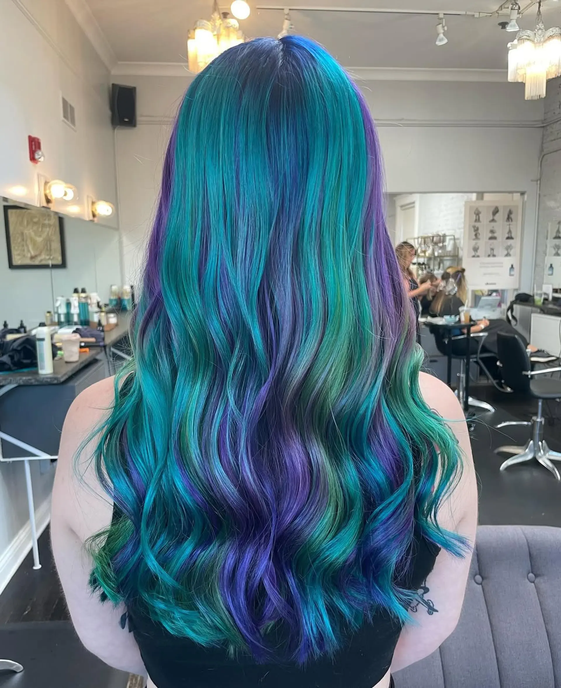A very long, wavy hairstyle characterized by soft, flowing waves cascading down the back. The look is achieved with a multidimensional fantasy color application. 1