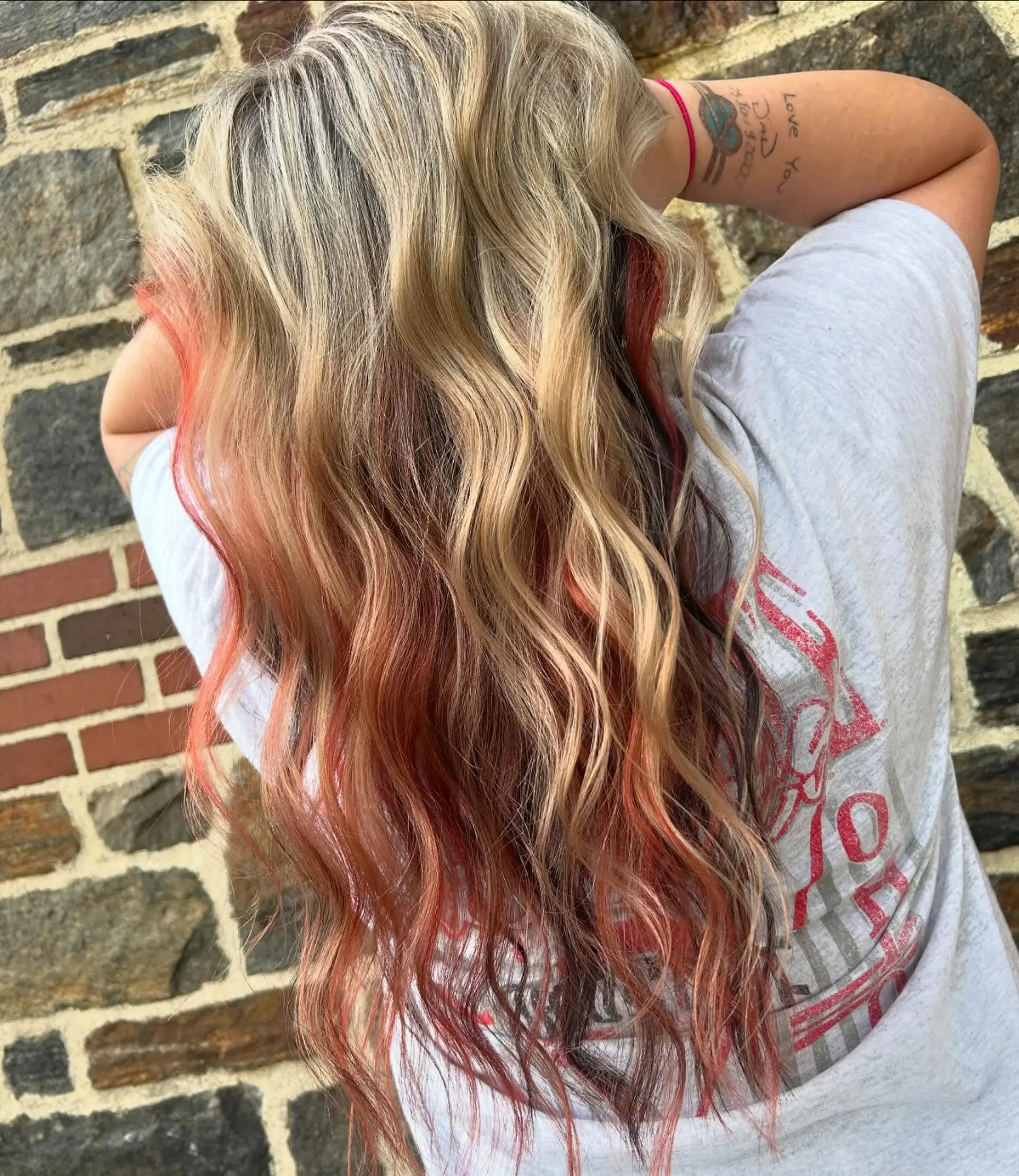 Long dimensional blonde hair styled in beachy waves with a contrasting red and dark peekaboo underlayer. 1