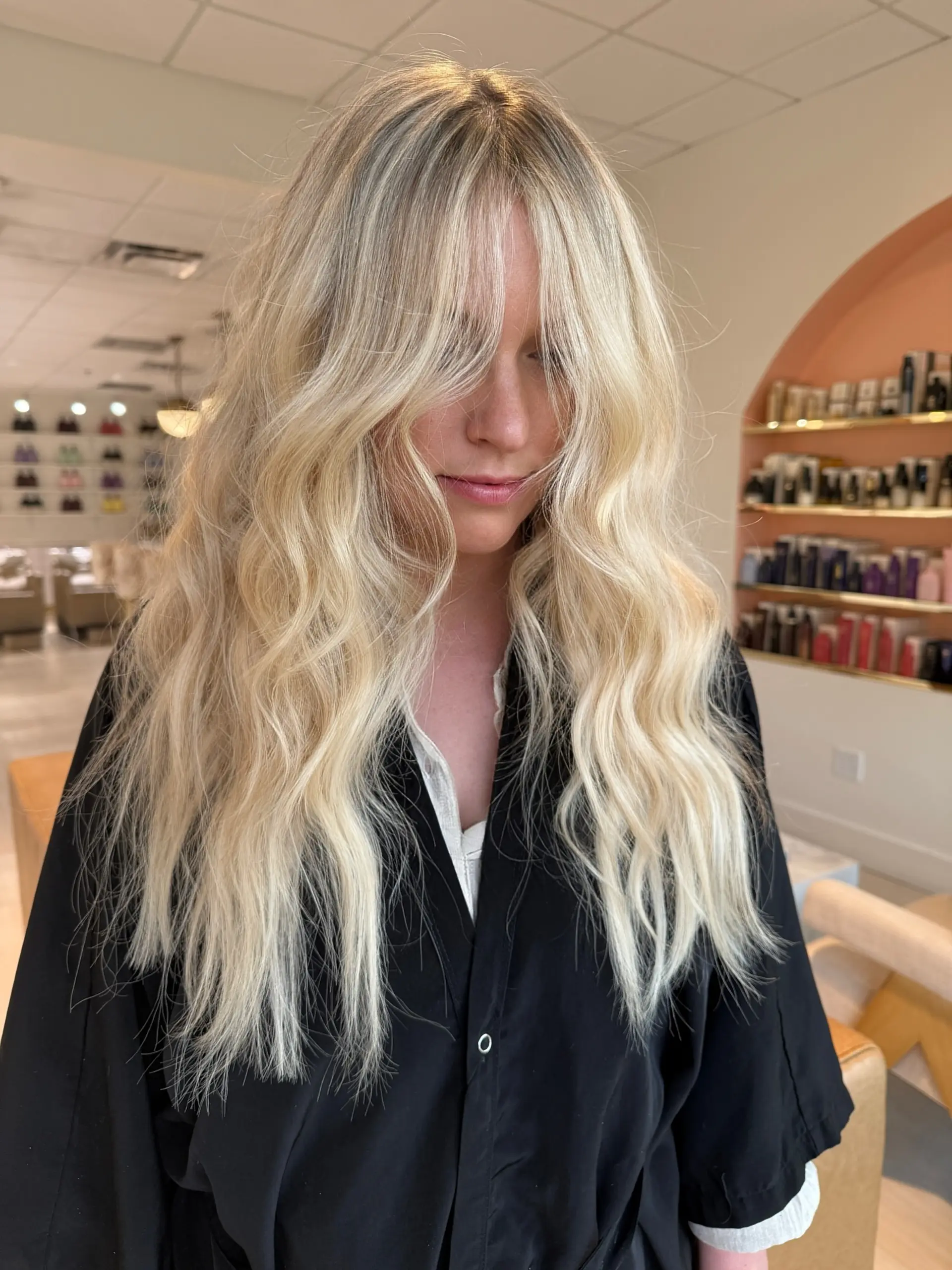 Long, textured bright blonde hair styled with loose beachy waves and face-framing curtain bangs. 1