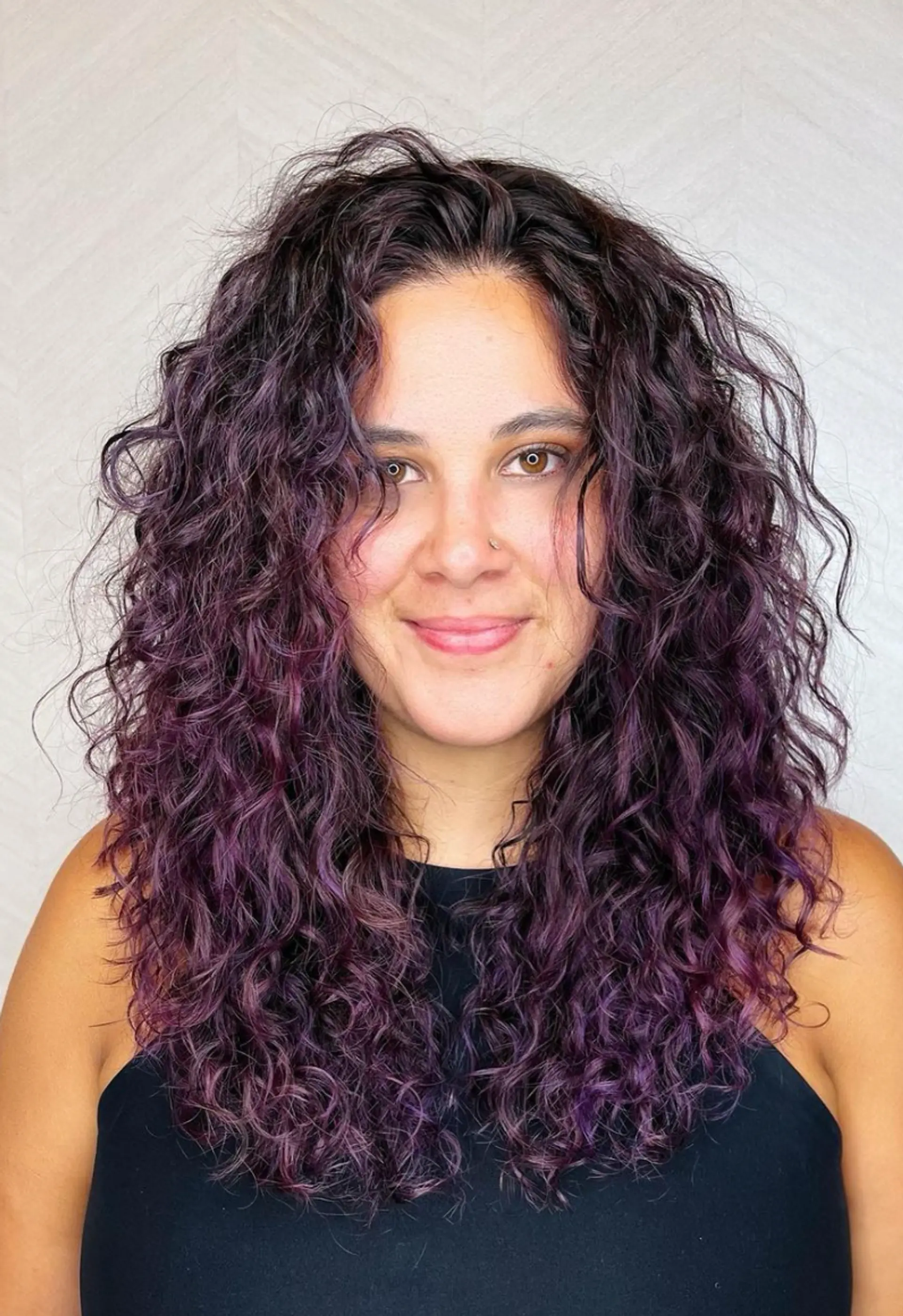 A long, voluminous, curly hairstyle with dark brown base and purple highlights, featuring naturally defined curls and textured, layered ends.

Color by @simabeautynyc
Cut and style by @juliamannino_hair
 1