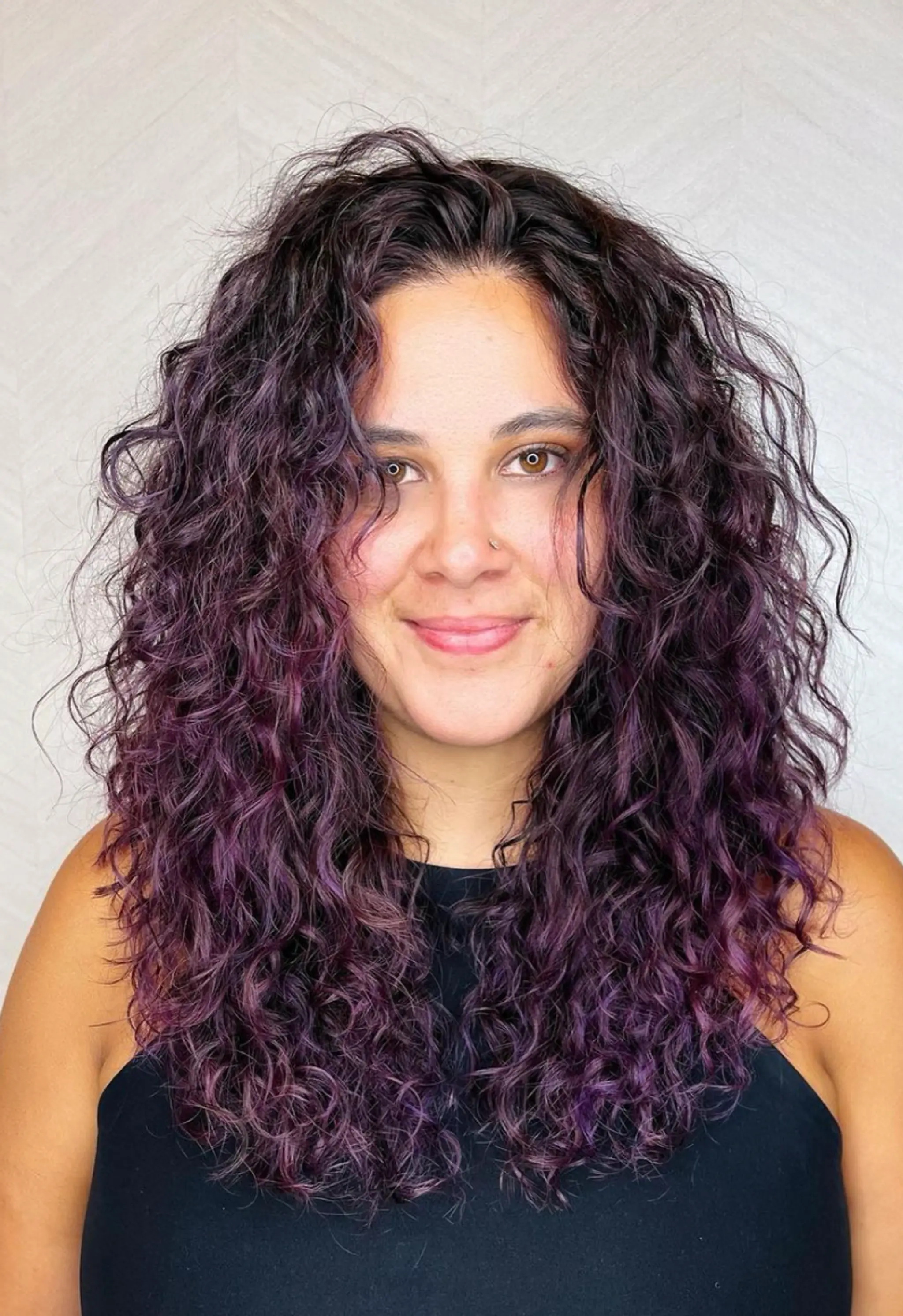 A long, voluminous, curly hairstyle with dark brown base and purple highlights, featuring naturally defined curls and textured, layered ends.

Color by @simabeautynyc
Cut and style by @juliamannino_hair
