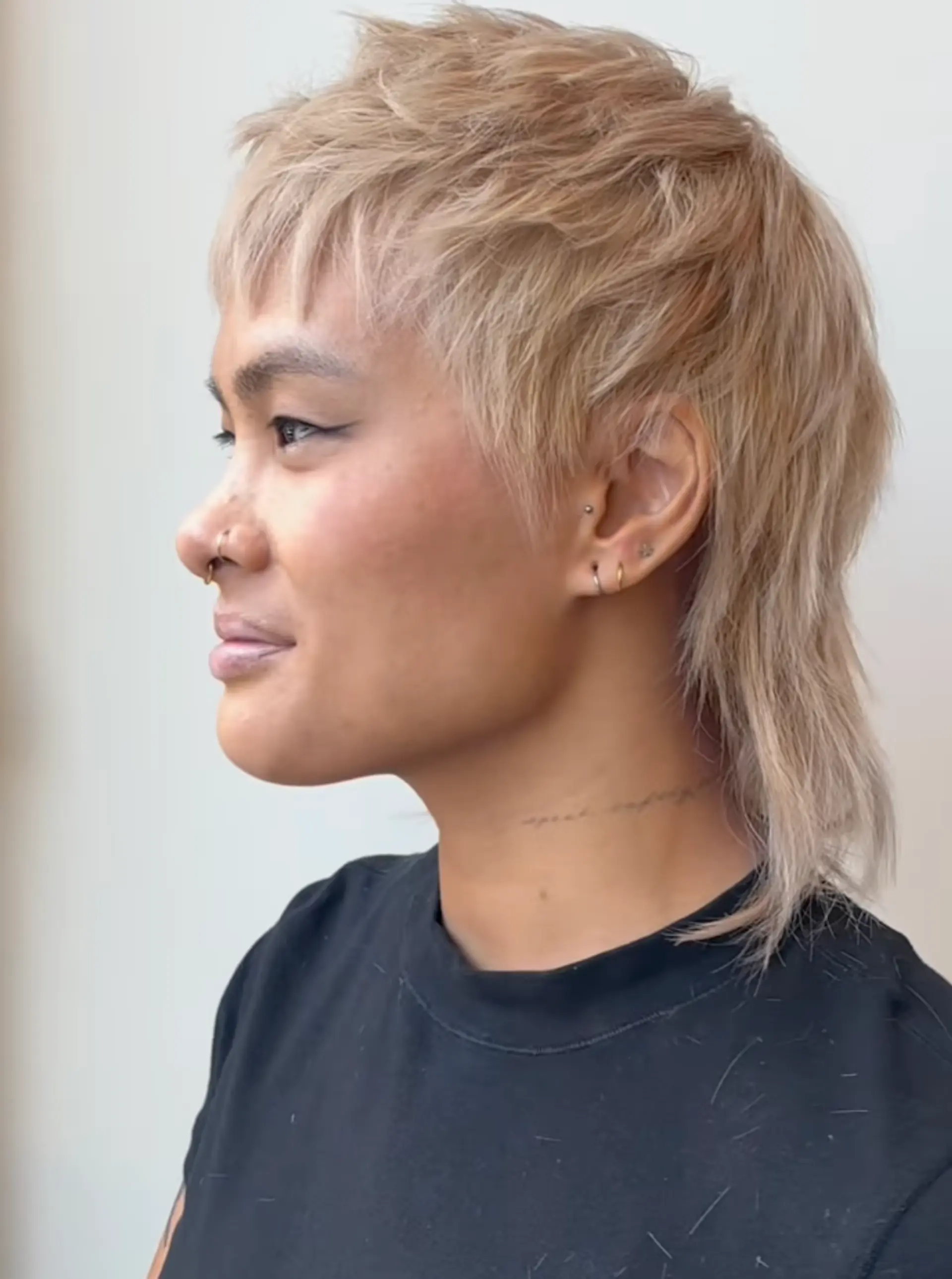 A short, edgy mullet cut with shaggy, wavy layers and blond color, featuring side swept bangs and longer strands at the nape. 1