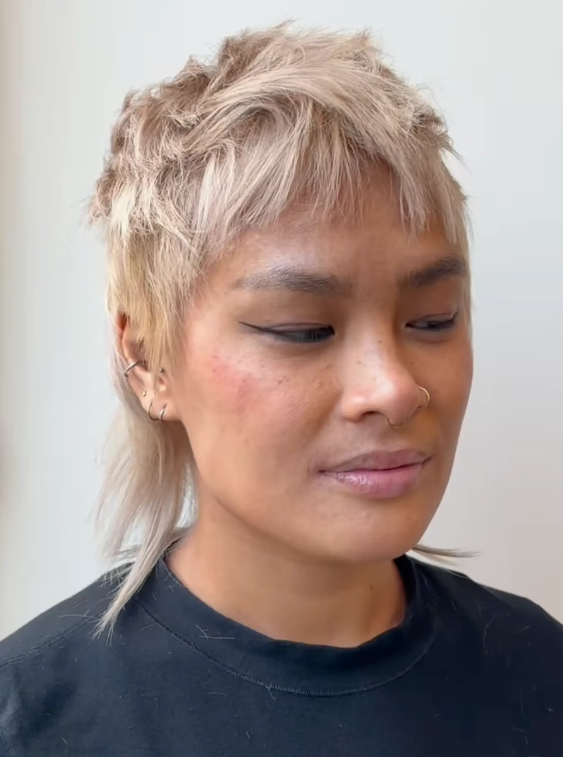 A short, edgy mullet cut with shaggy, wavy layers and blond color, featuring side swept bangs and longer strands at the nape. 2