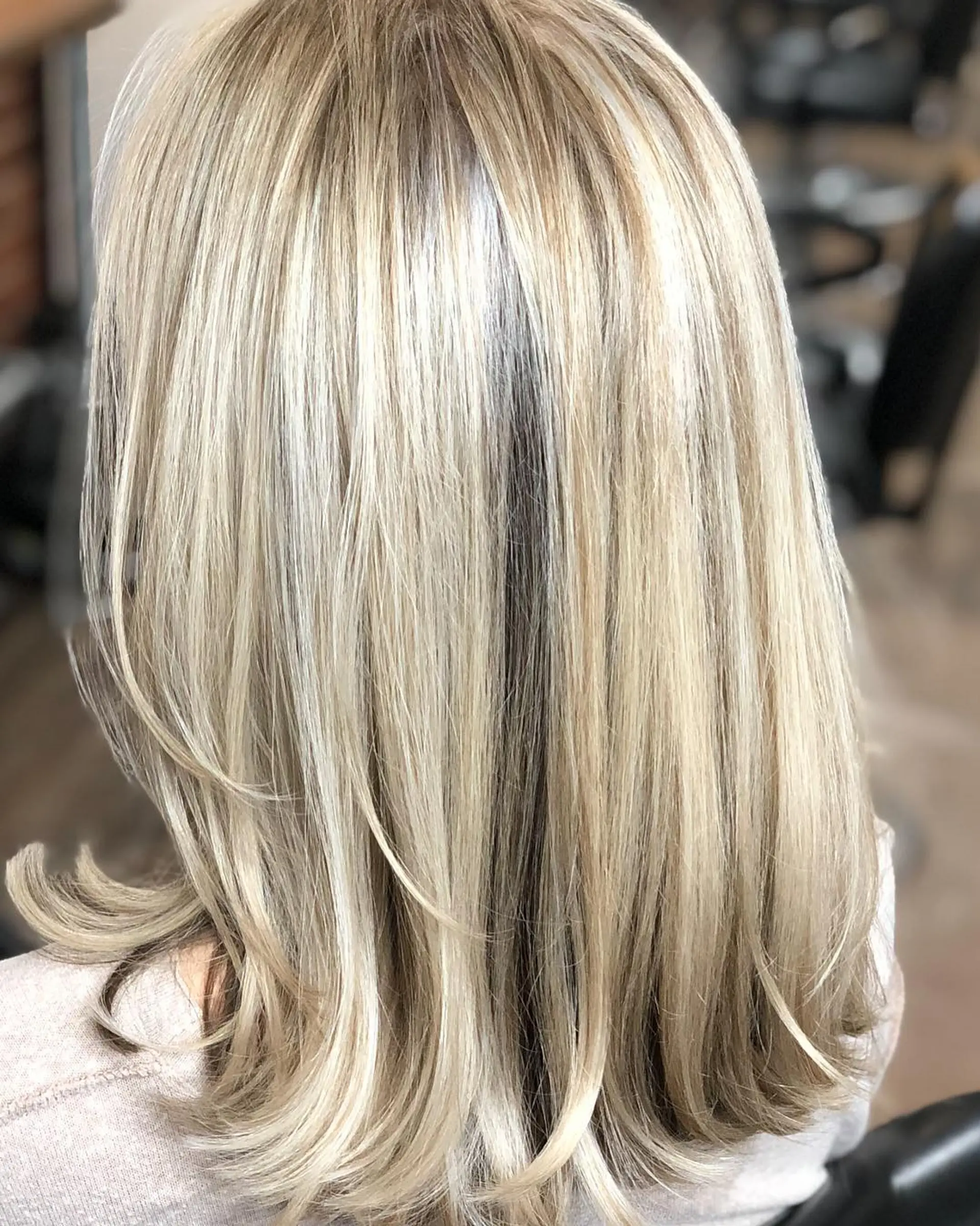 Medium-length straight hair styled with subtle flipped ends, showcasing dimensional cool blonde hair painting. 1