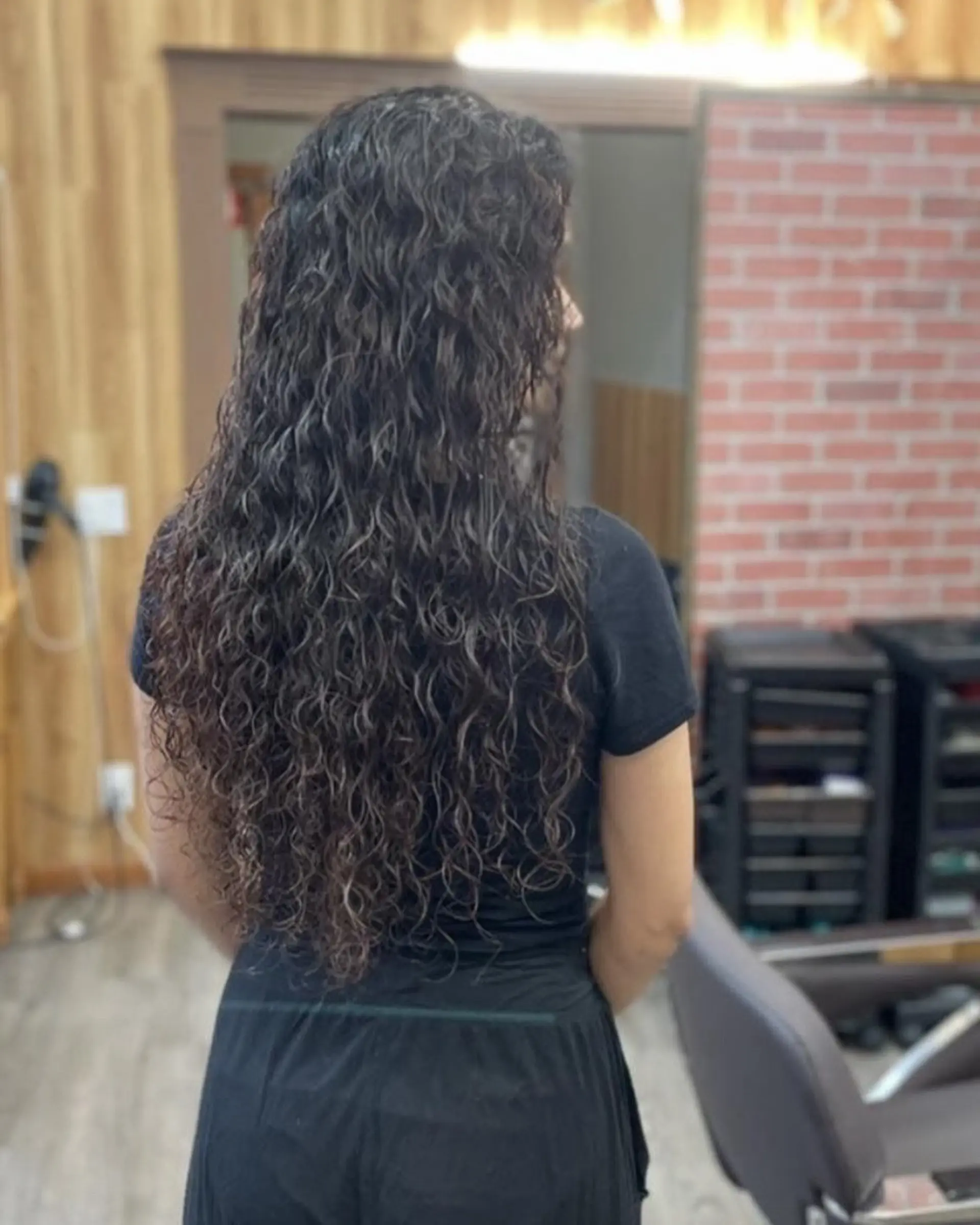 Long dark hair styled with defined, textured curls flowing down the back. 1