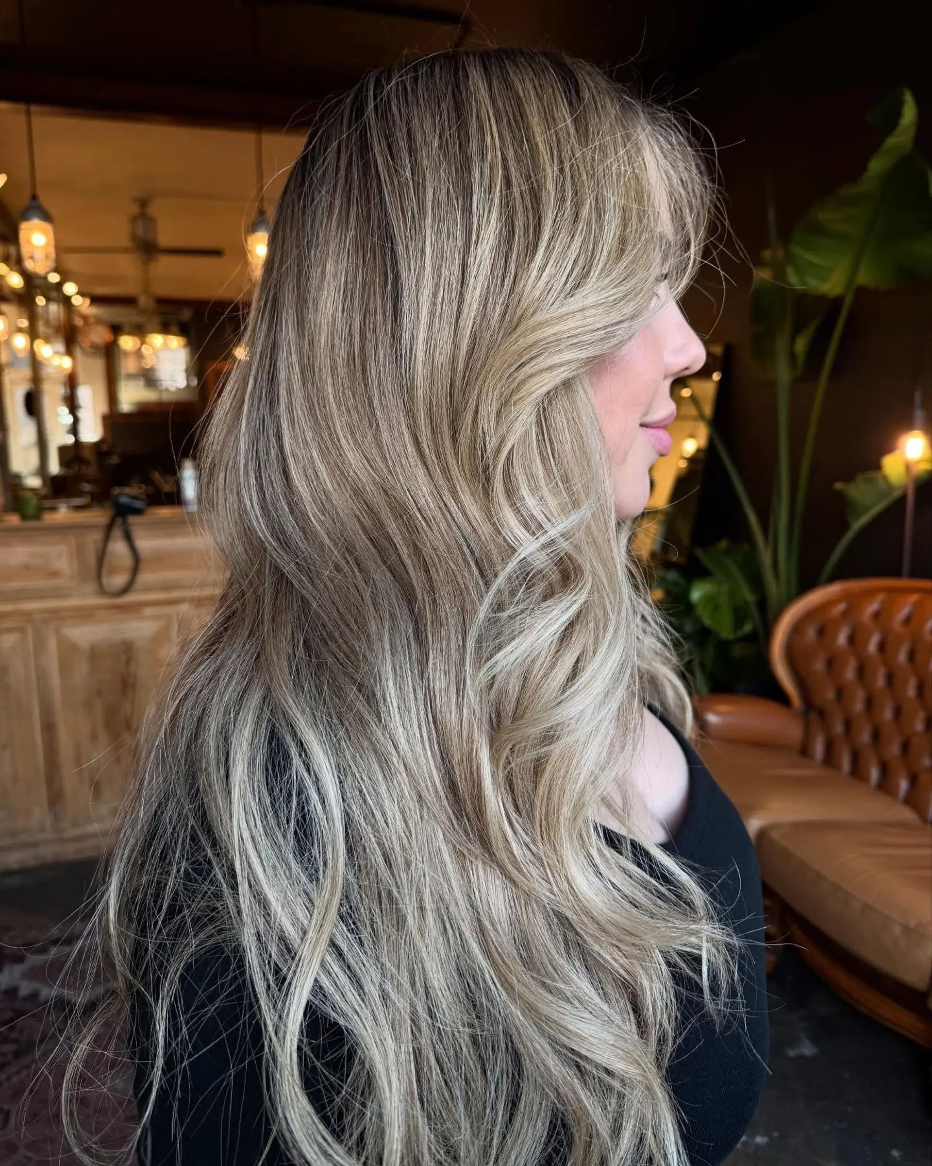 Long cascading blonde hair styled with soft loose waves and dimensional full highlights with face-framing pieces. 1